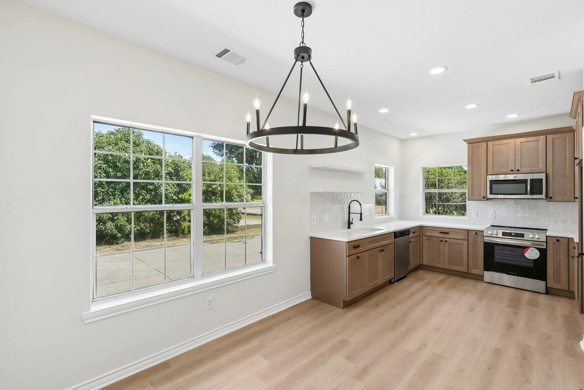 Open-concept kitchen and dining area featuring wood-finish flooring, recessed lighting, and a modern chandelier