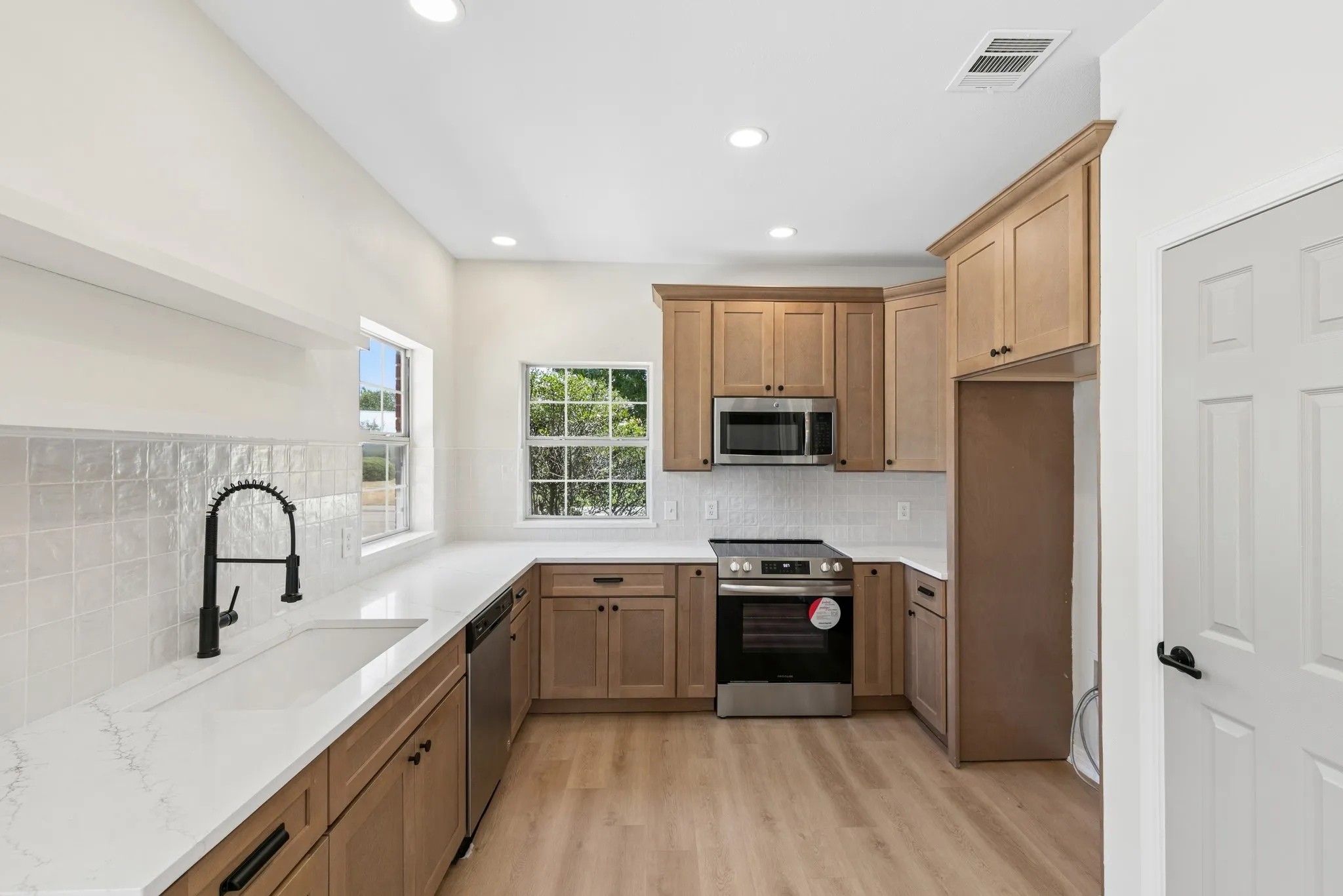 Kitchen featuring wood-finish cabinetry, stainless steel appliances, white subway tile backsplash, recessed lighting, and wood-finish flooring
