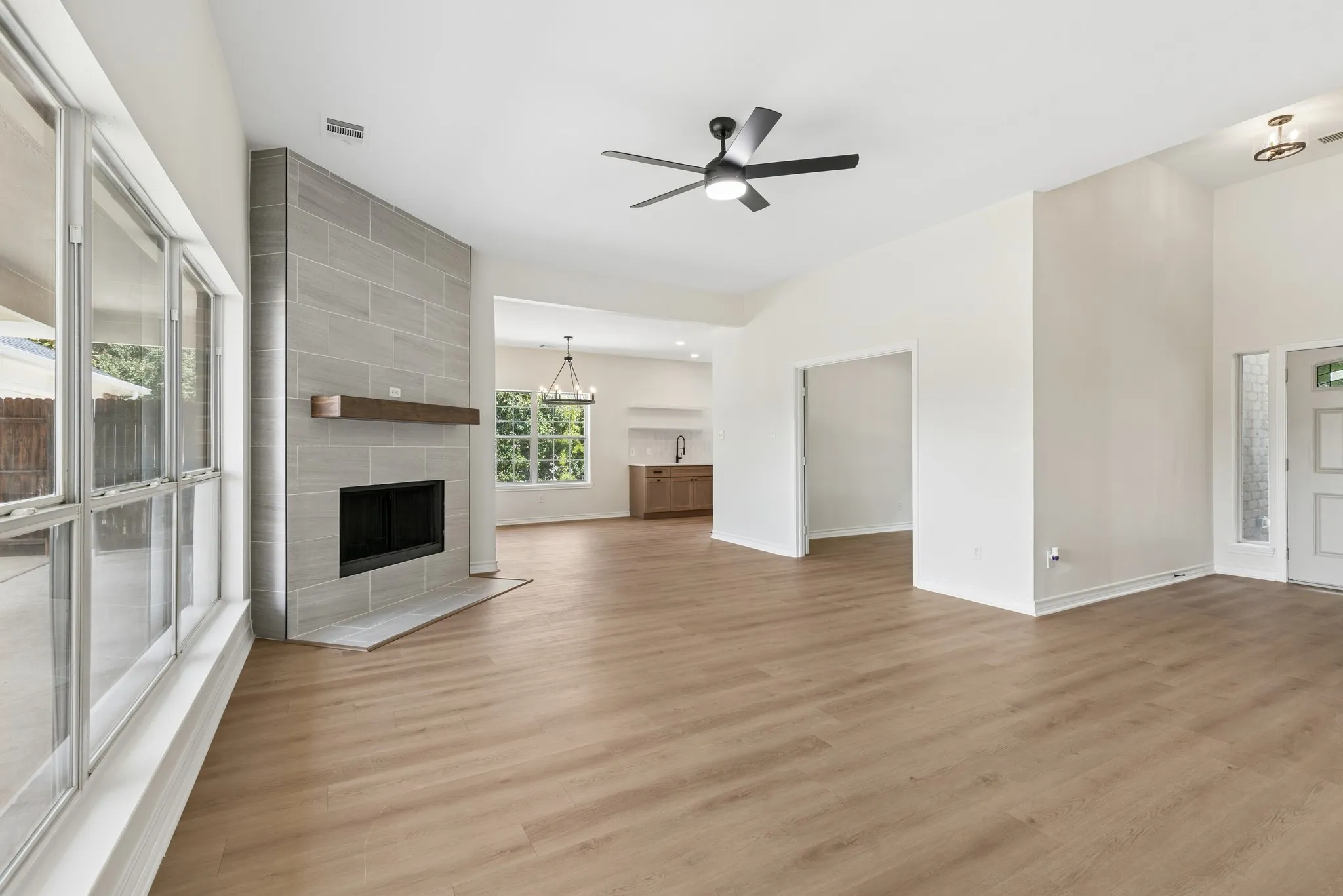 Spacious room featuring wood-finish flooring, a contemporary fireplace with a wood mantle and tile surround, and expansive windows