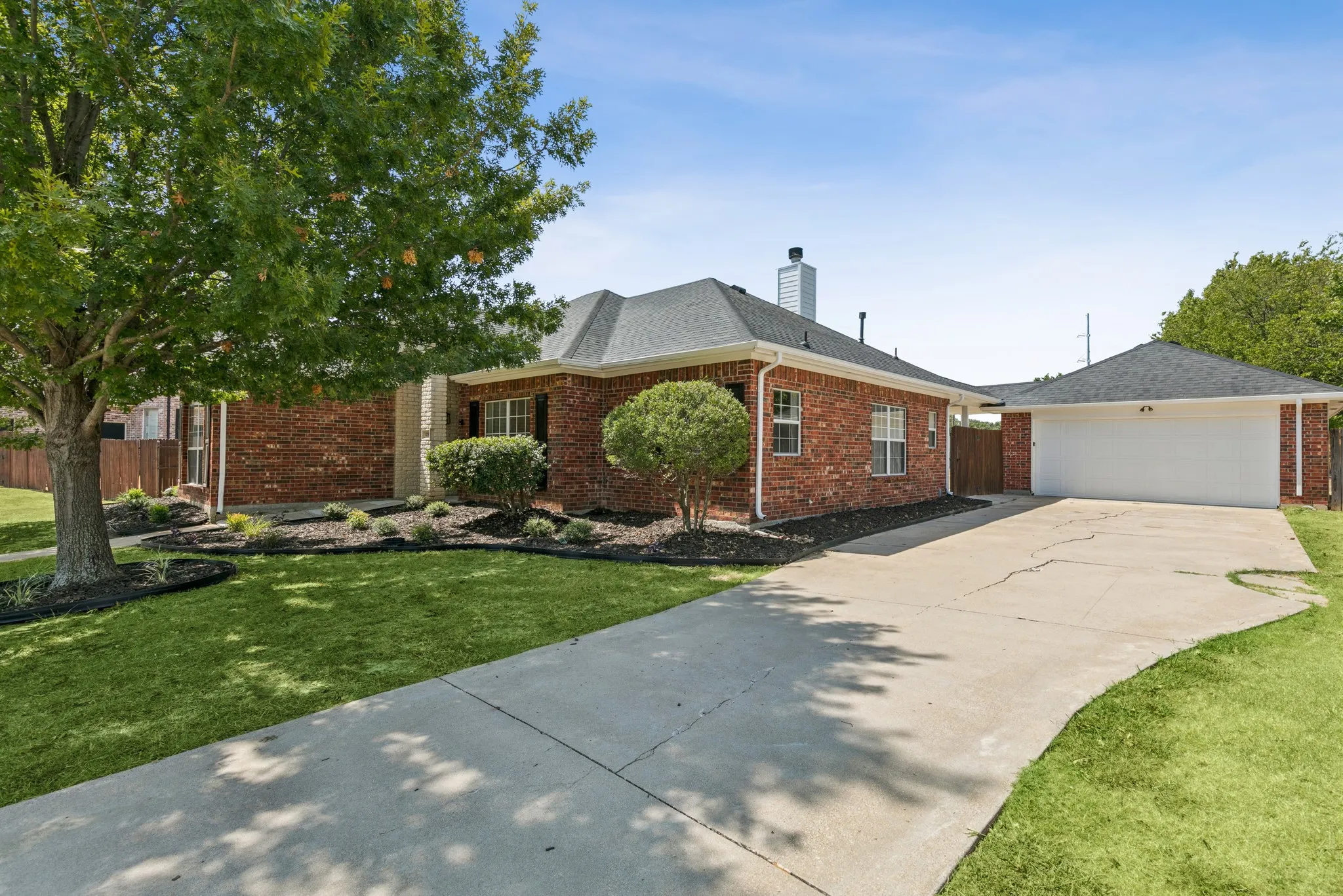 Brick exterior with a detached garage, concrete driveway, and mature landscaping