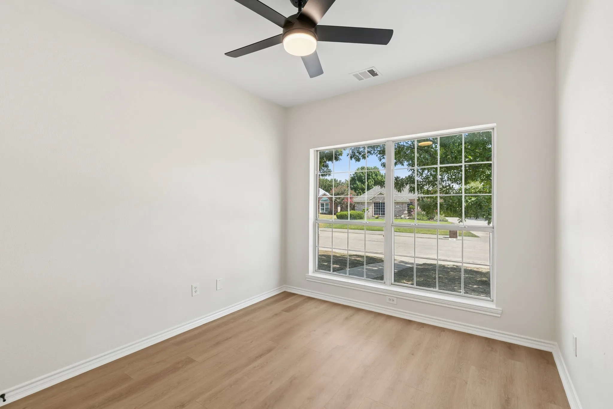 Wood-finish flooring, white painted walls, large multi-pane window, and a ceiling fan with integrated lighting