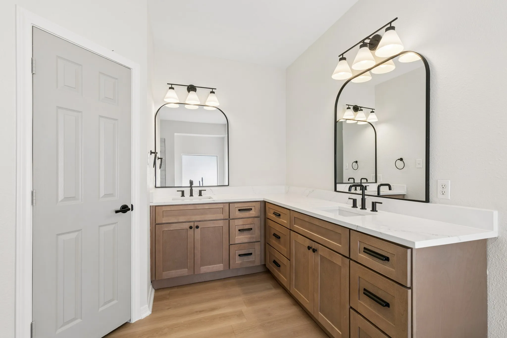 Dual vanity with wood-finish cabinetry, white countertops, and black fixtures