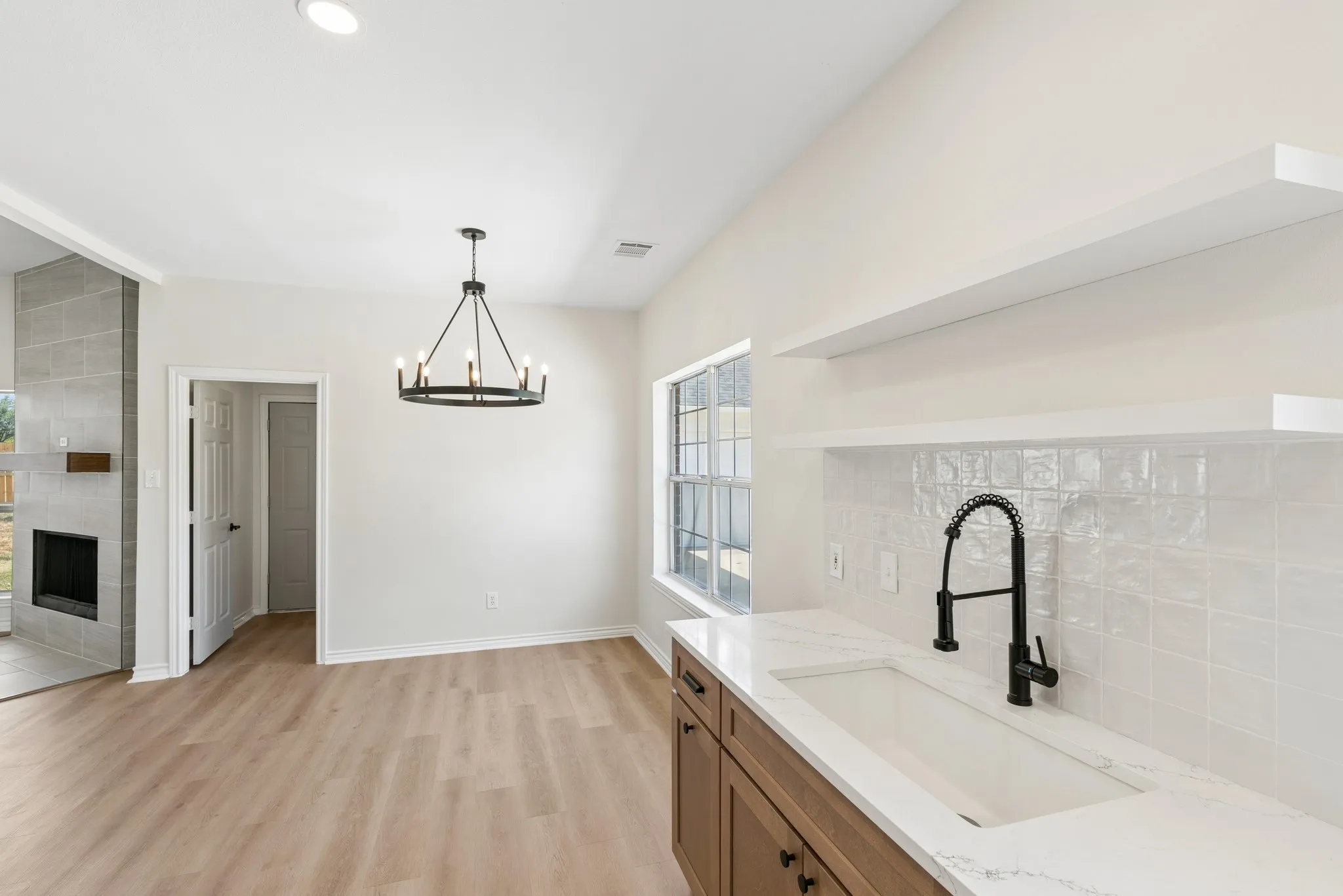 Vaulted ceilings, wood-finish flooring, fireplace with stone surround, kitchen with white countertop, and white tile backsplash