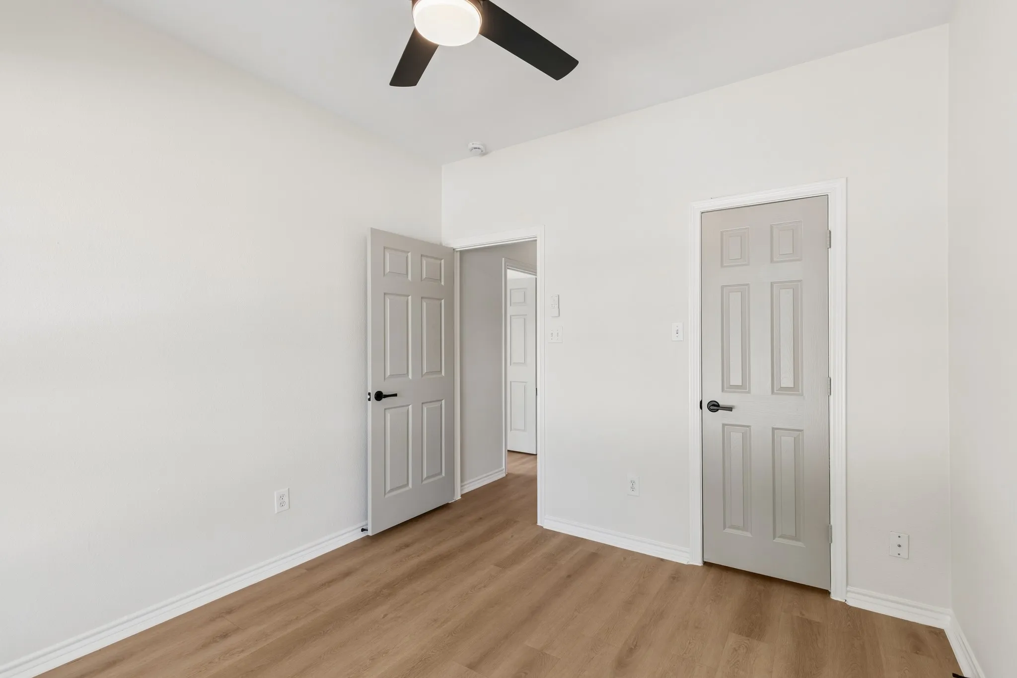 Wood-finish flooring throughout, white walls, and a ceiling fan with integrated lighting