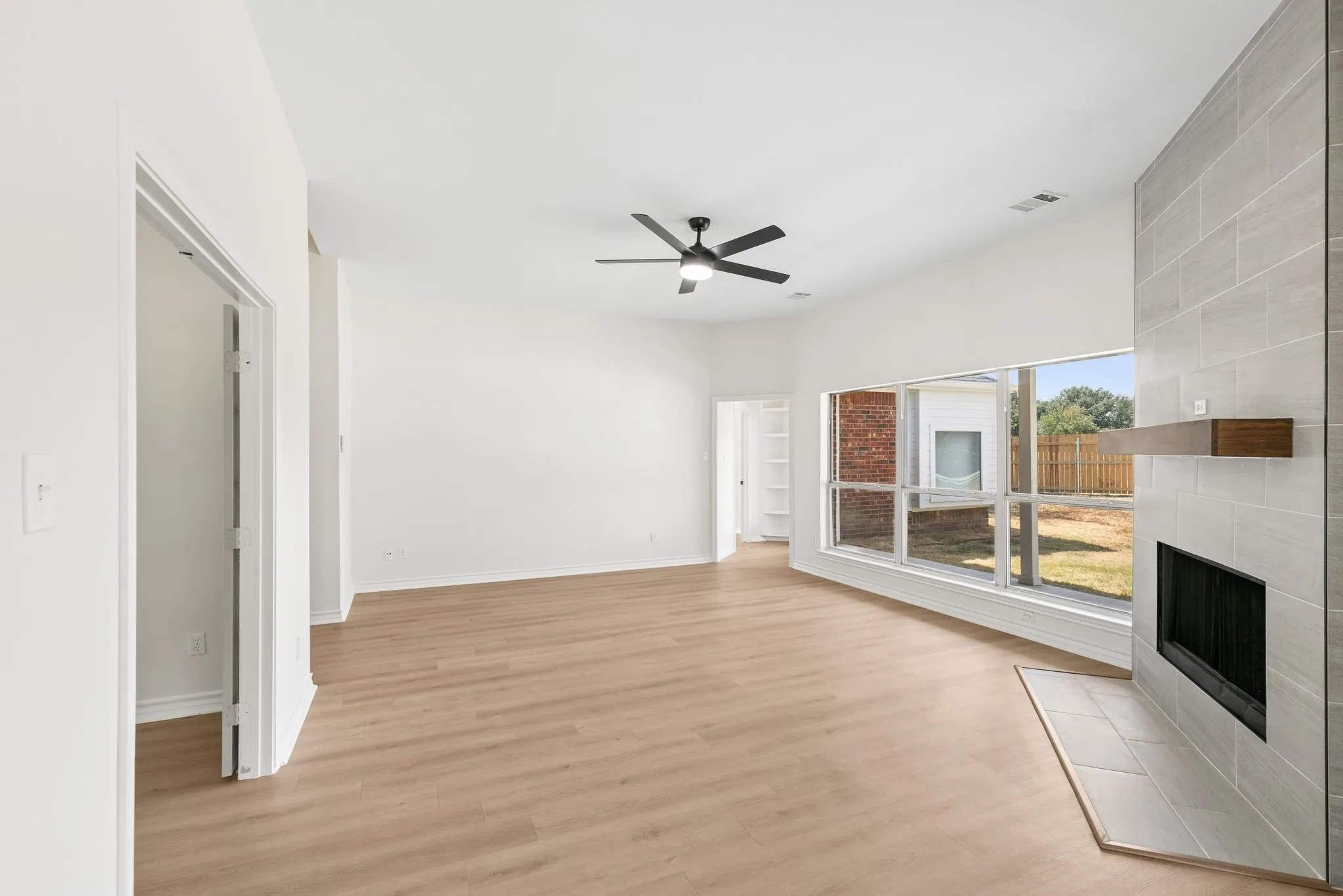 Spacious room featuring wood-finish flooring, a contemporary ceiling fan, and a tiled fireplace with a wood mantle