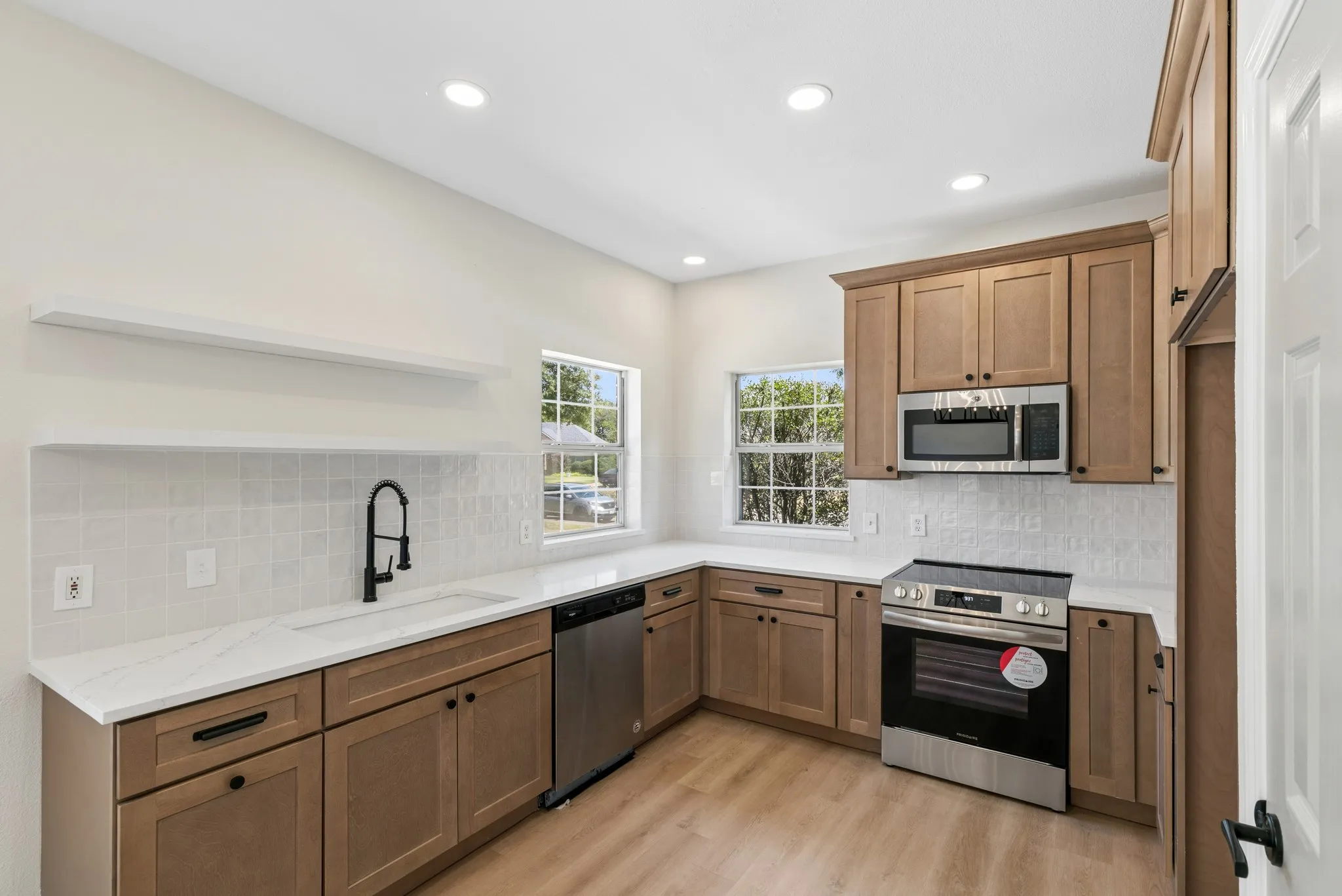 Kitchen featuring wood-finish cabinetry, white countertops, stainless steel appliances, and a tiled backsplash