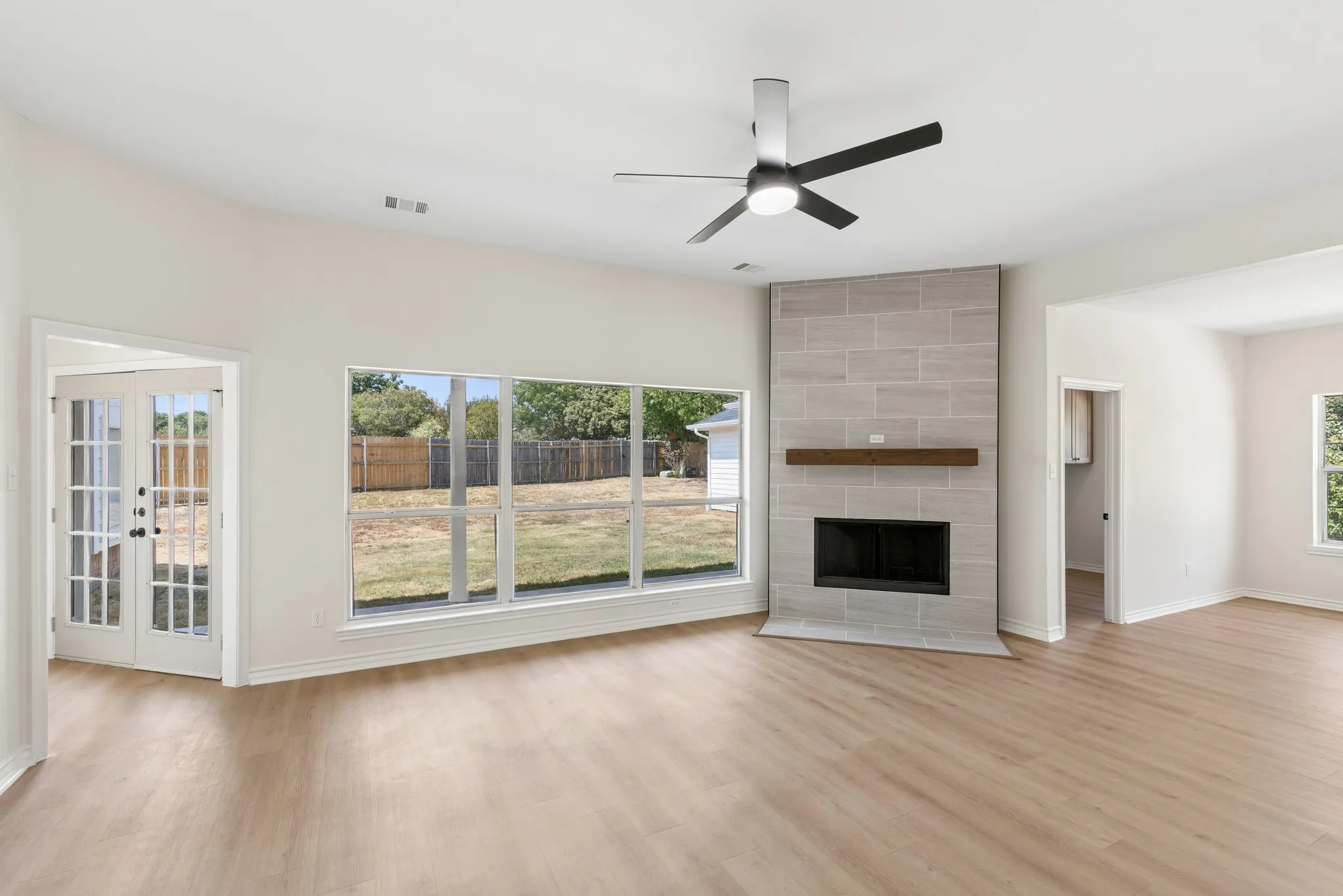 Spacious room featuring wood-finish flooring, a tile-surround fireplace with a wood mantel, a ceiling fan, and large windows