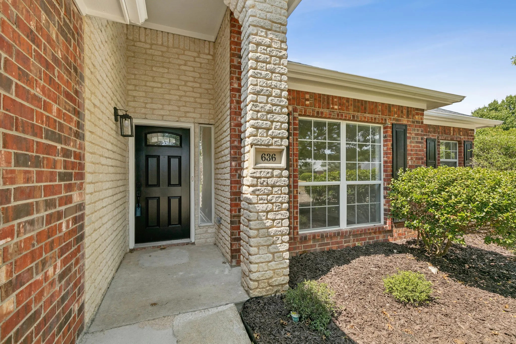 Brick and stone exterior with a black paneled door featuring a decorative glass insert