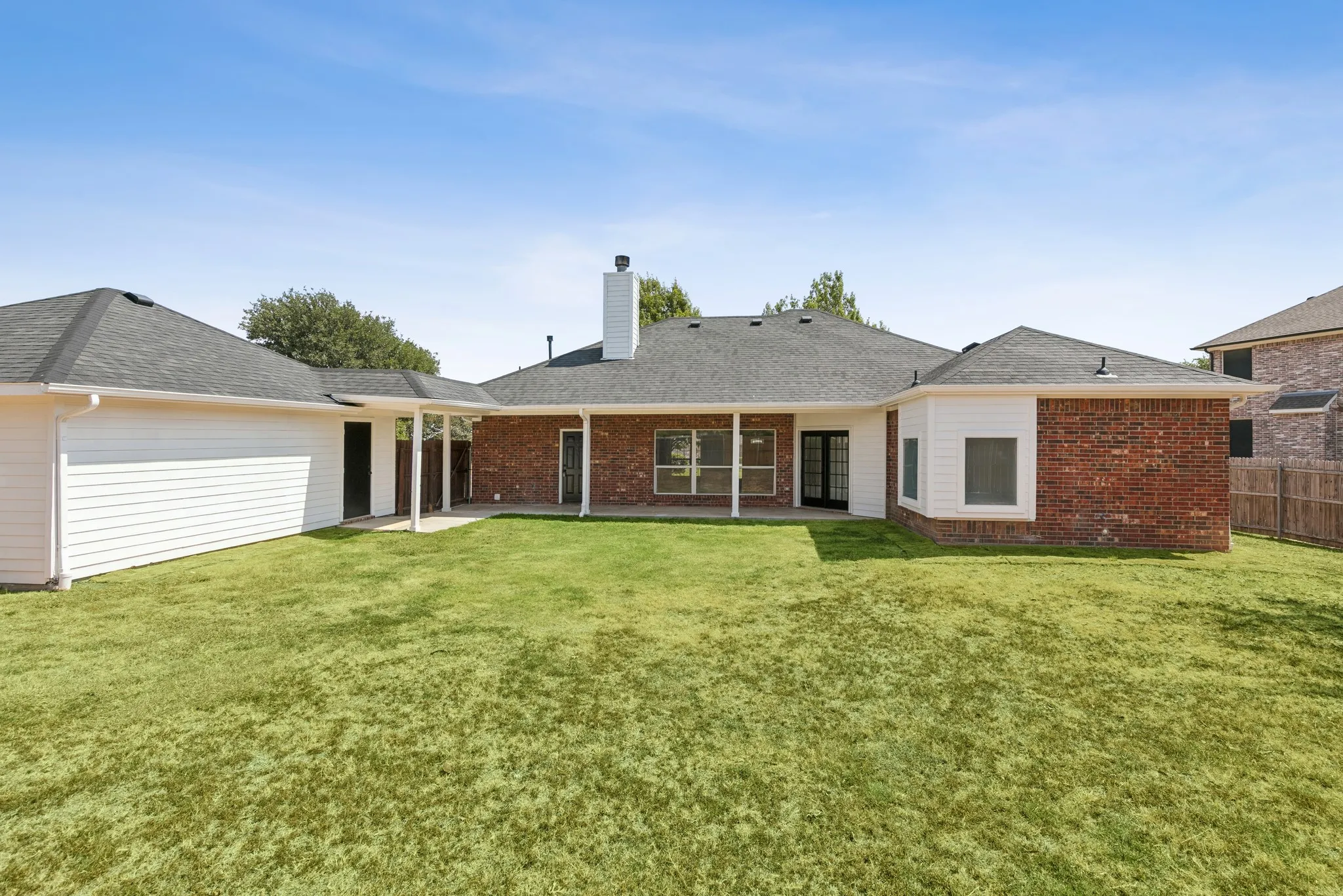 Brick and siding exterior with a covered patio and expansive lawn