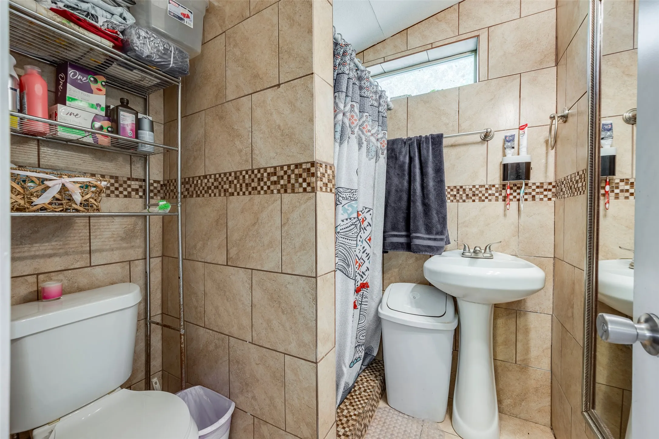 Floor-to-ceiling tile in a neutral tone with a decorative accent band, pedestal sink, and built-in toilet