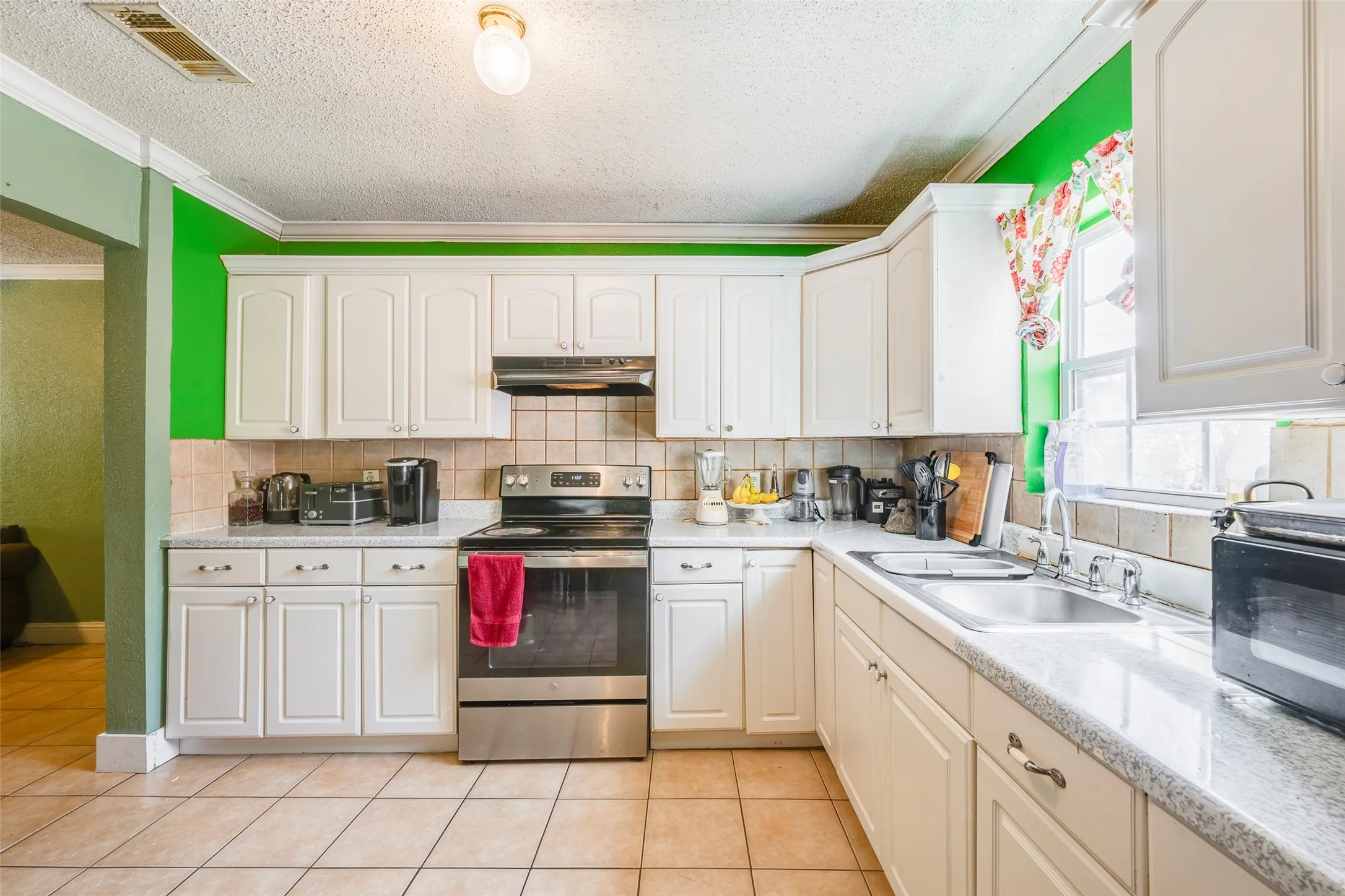 White cabinetry, stone-finish countertops, stainless steel range with overhead microwave, tiled backsplash, and tile flooring