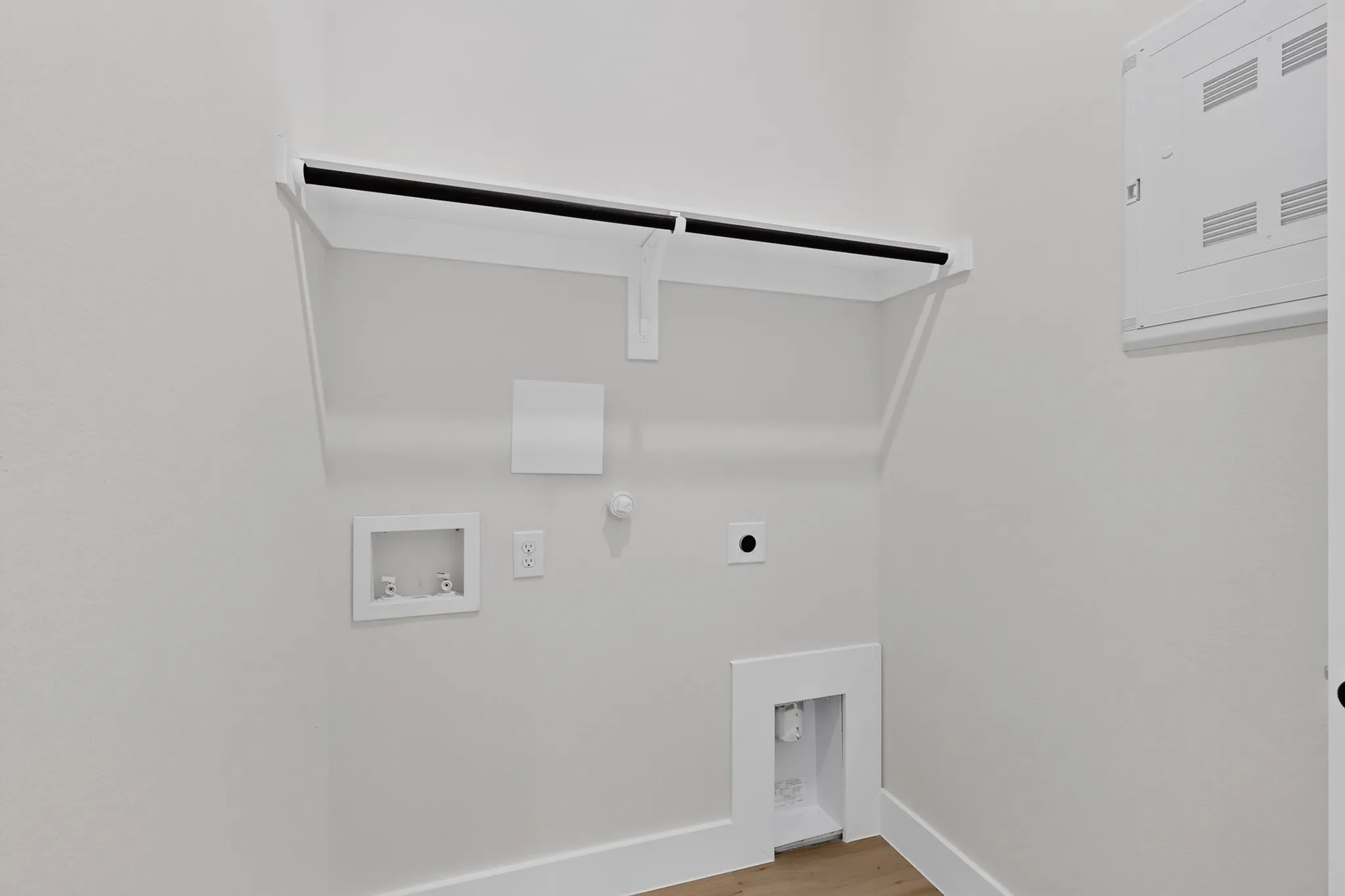 Laundry area with an upper storage shelf, utility hookups, and wood-finish flooring