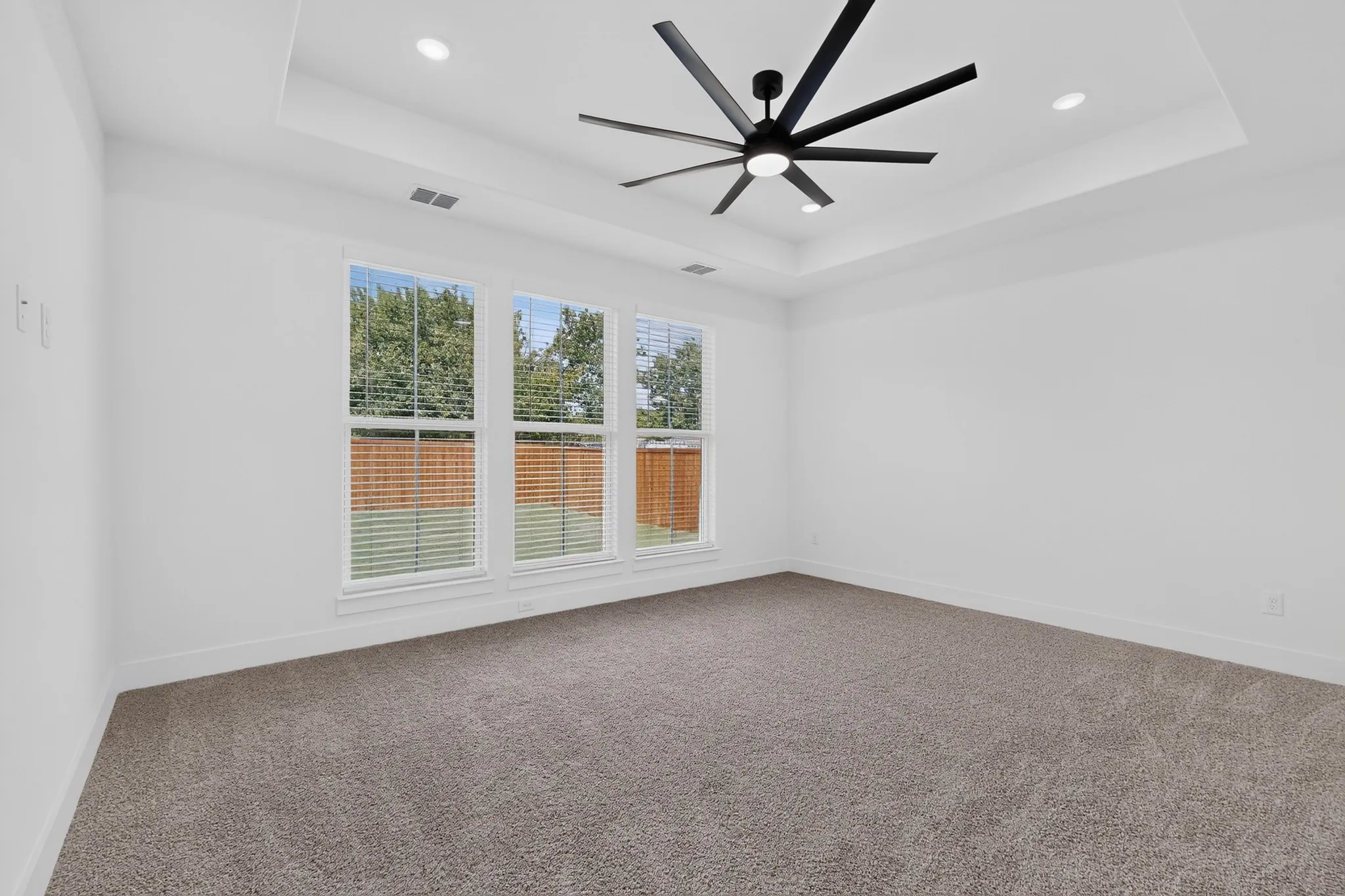 Tray ceiling featuring recessed lighting and a ceiling fan, three windows with blinds, and carpeted flooring