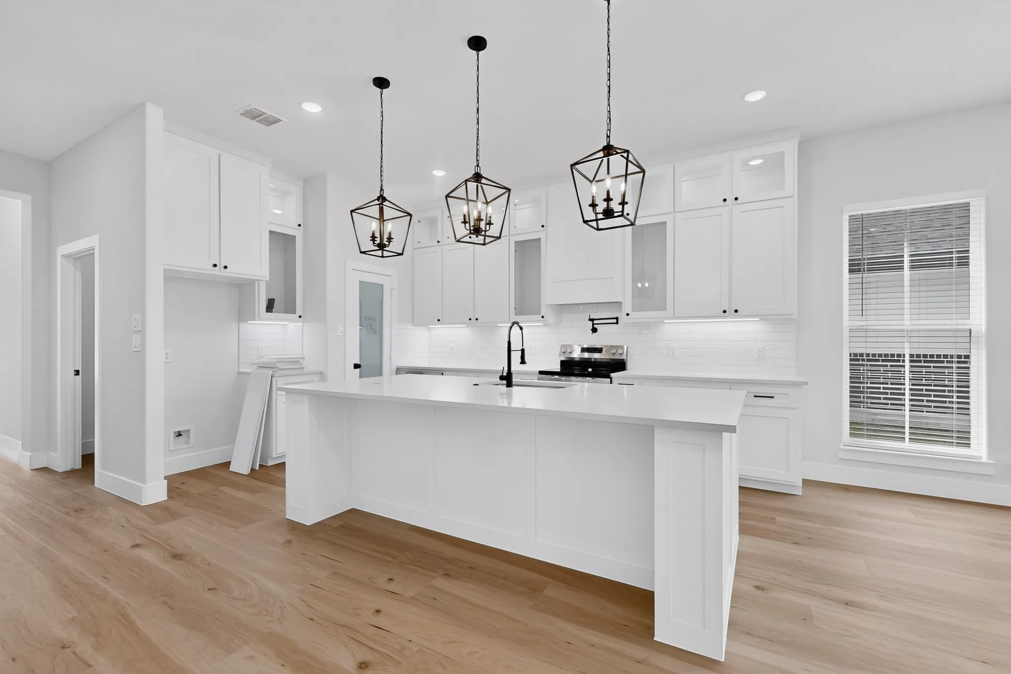 Kitchen featuring white cabinetry, a large center island, wood-finish flooring, white subway tile backsplash, and black pendant lighting