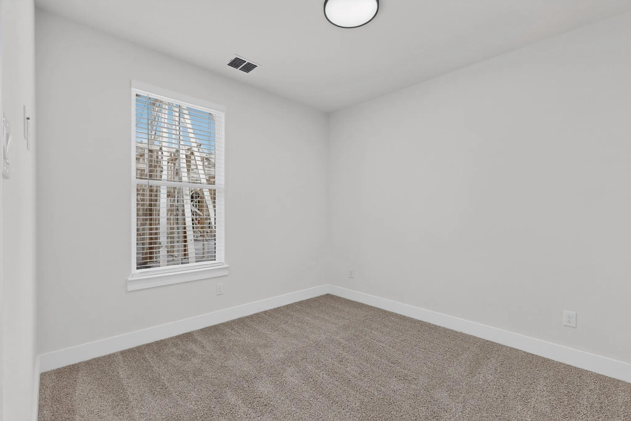 Neutral-toned carpet flooring, white painted walls, window with blinds, and a flush-mount ceiling light