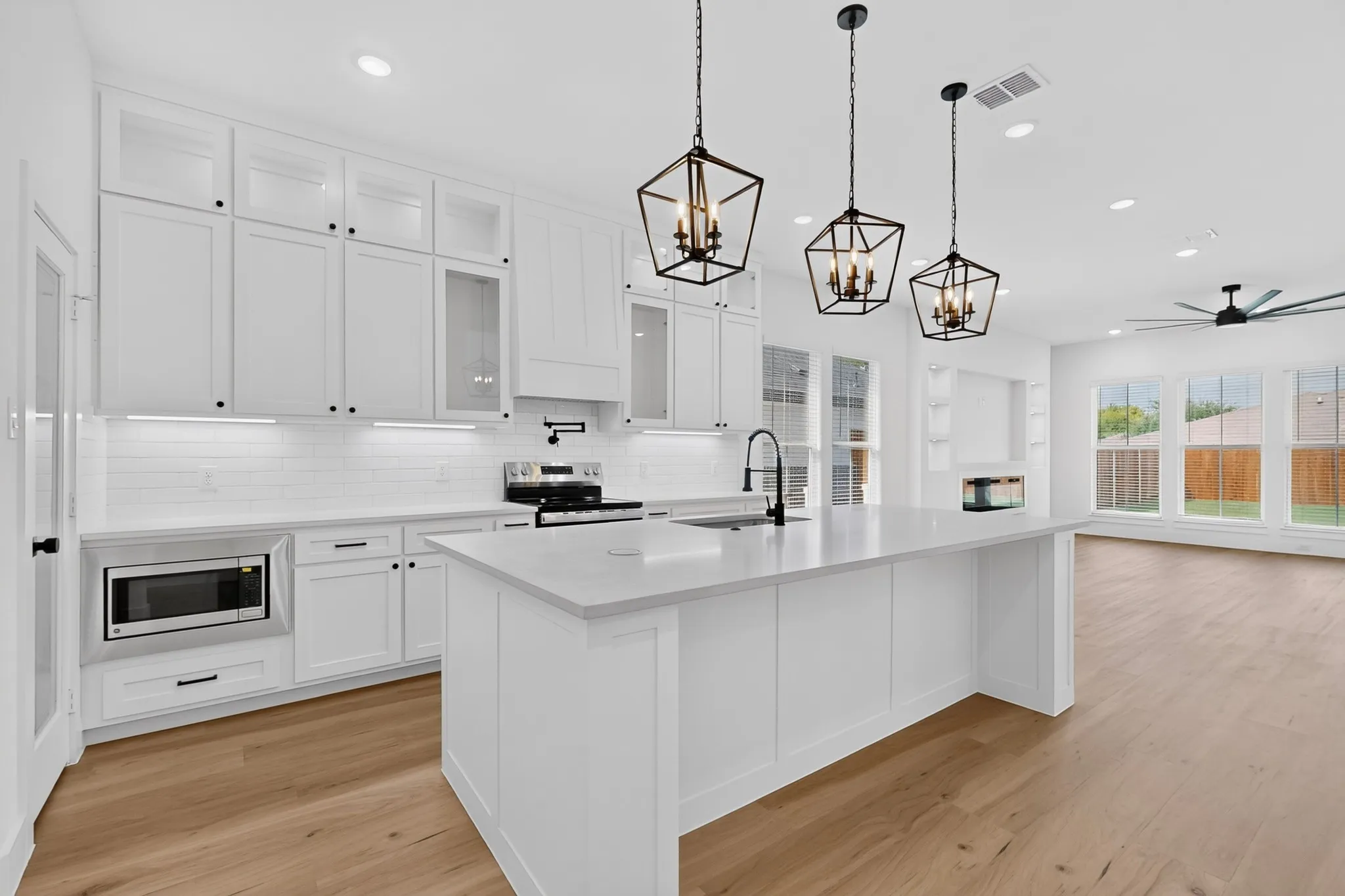 Kitchen featuring a large island with an integrated sink, white cabinetry, subway tile backsplash, and light wood-finish flooring