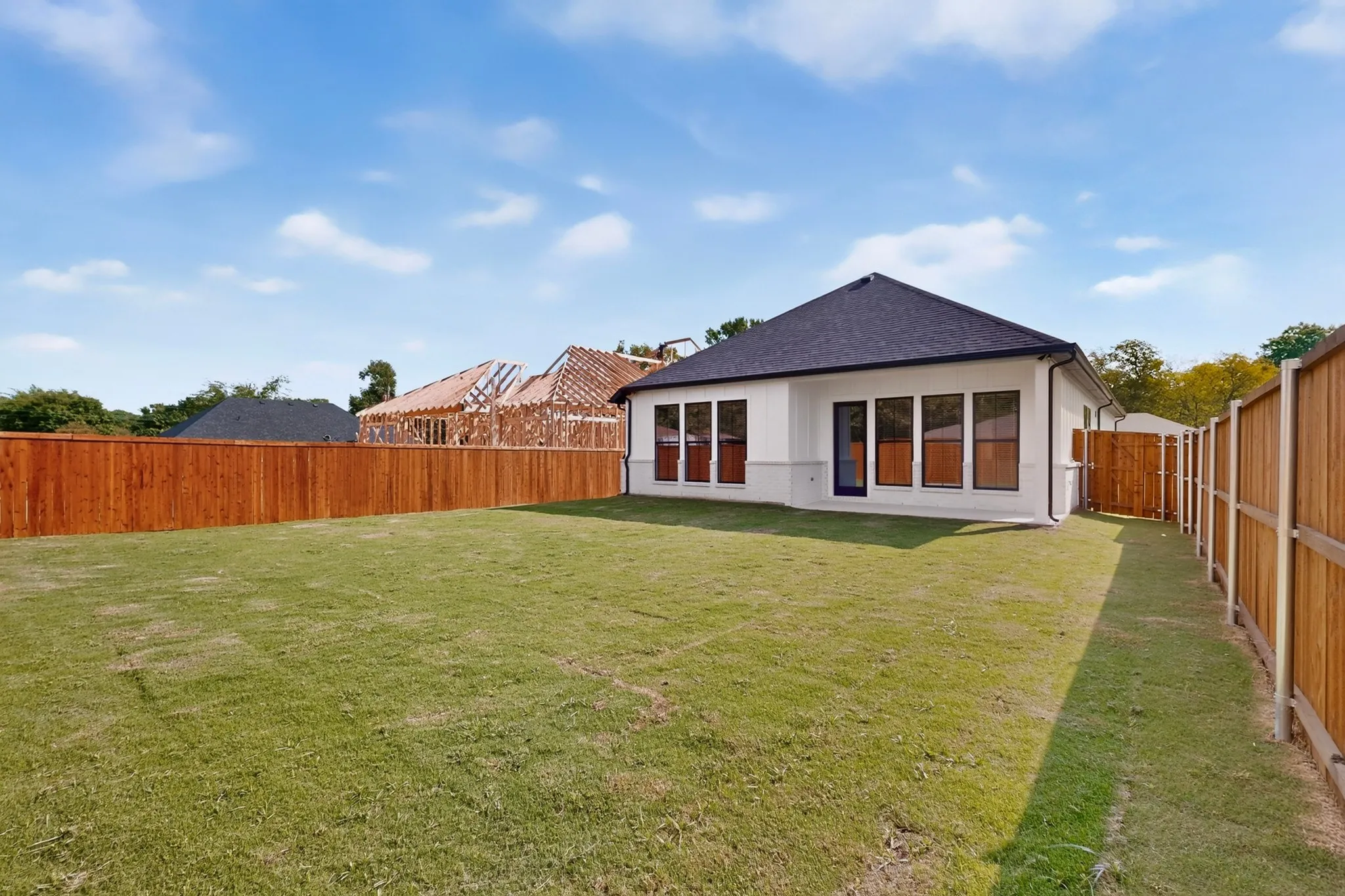 Expansive backyard with a manicured lawn, dark shingle roof, and a wood privacy fence
