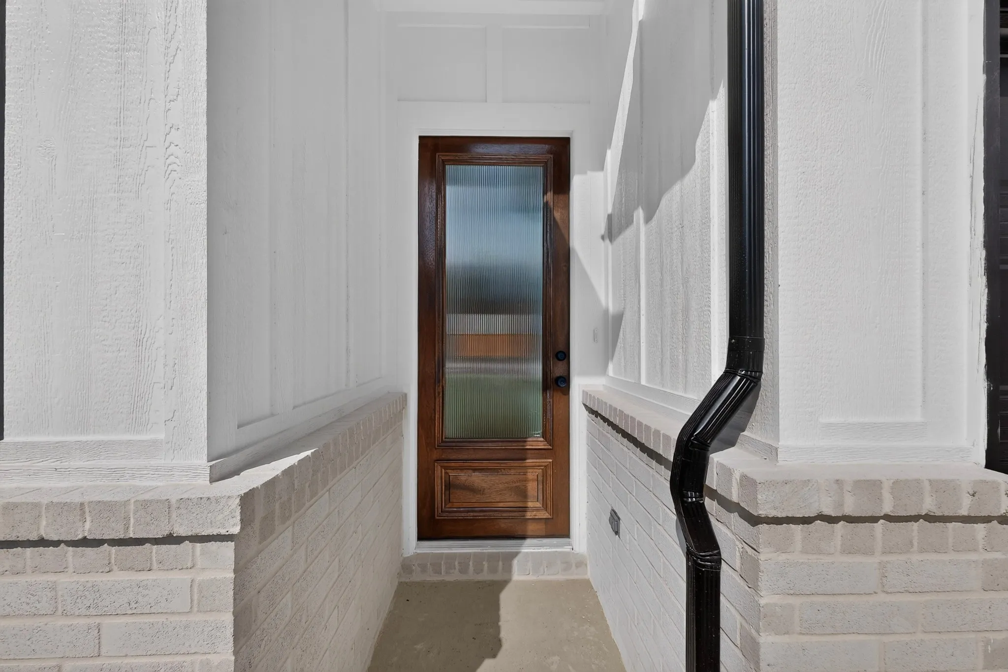 Wood-panel entry door with frosted glass insert, flanked by white board and batten siding, and light brick base