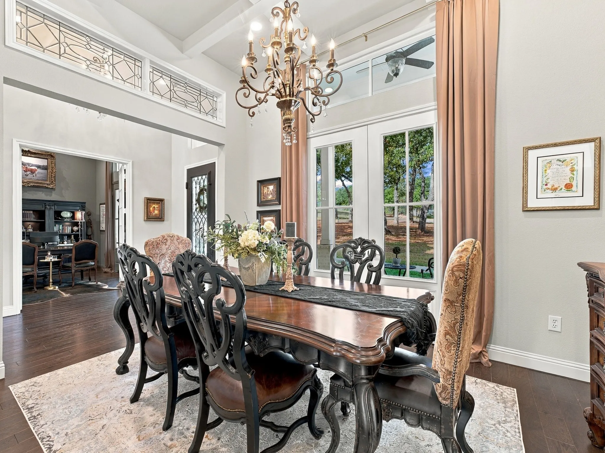 Soaring ceilings with exposed beams, decorative transom windows, dark wood-finish flooring, and French doors leading to an outdoor area