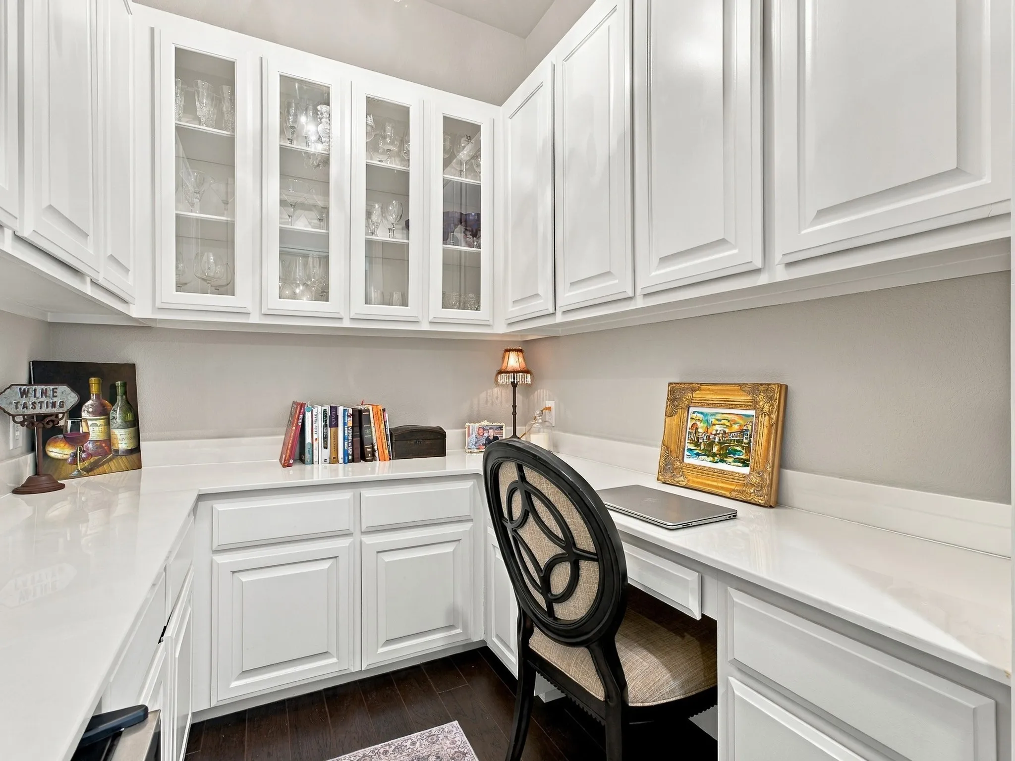 Built-in desk area with white cabinetry, glass-front upper cabinets, light-toned countertop, and dark wood-finish flooring