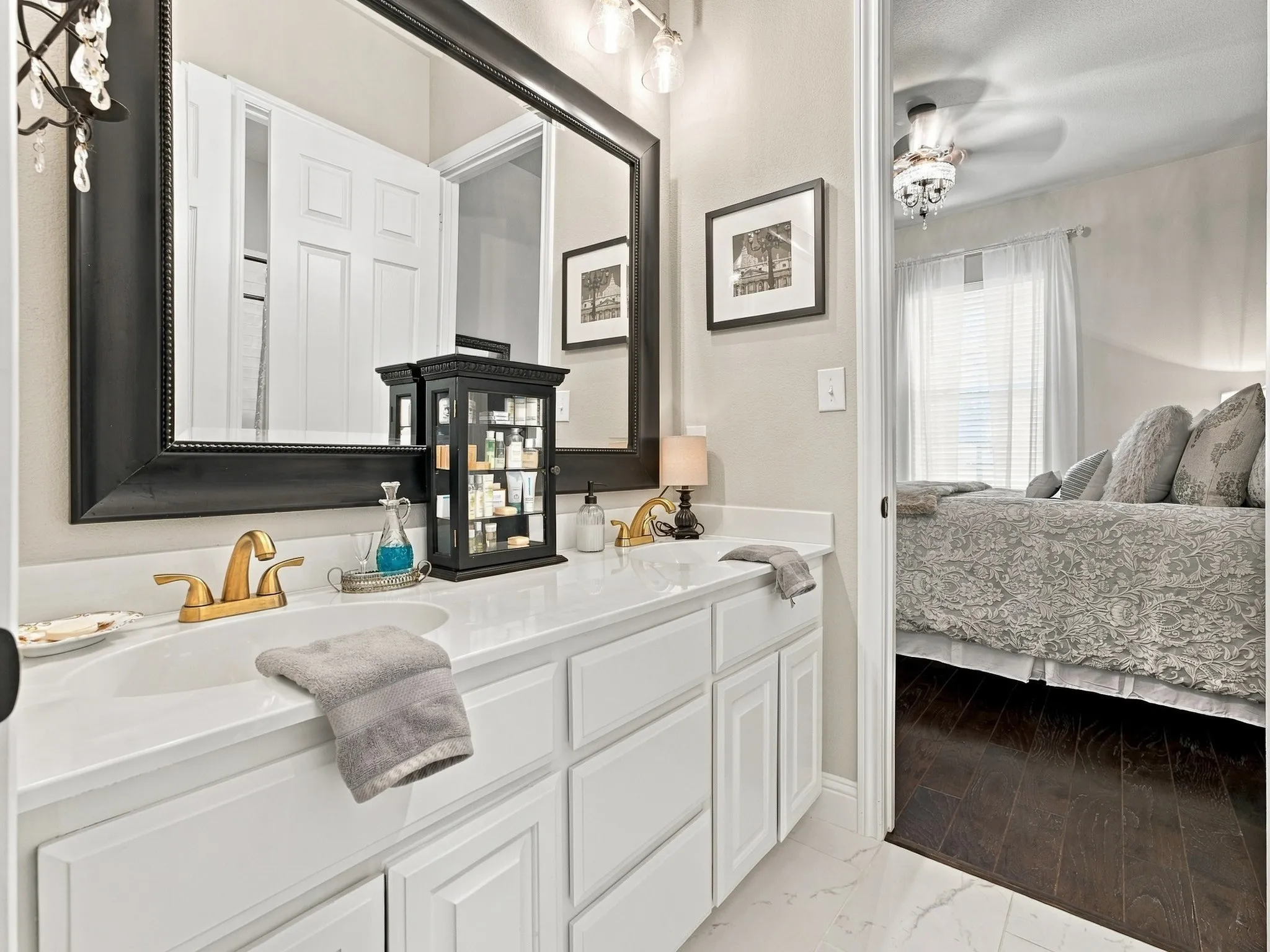 This Jack and Jill bath features dual vanity, white cabinetry and countertops, gold-finish fixtures, and a large framed mirror