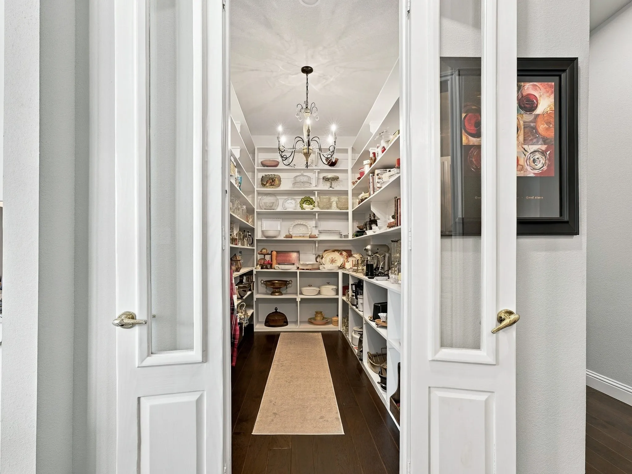 Walk-in pantry featuring extensive built-in shelving, dark wood-finish flooring, a decorative chandelier, and paneled French doors