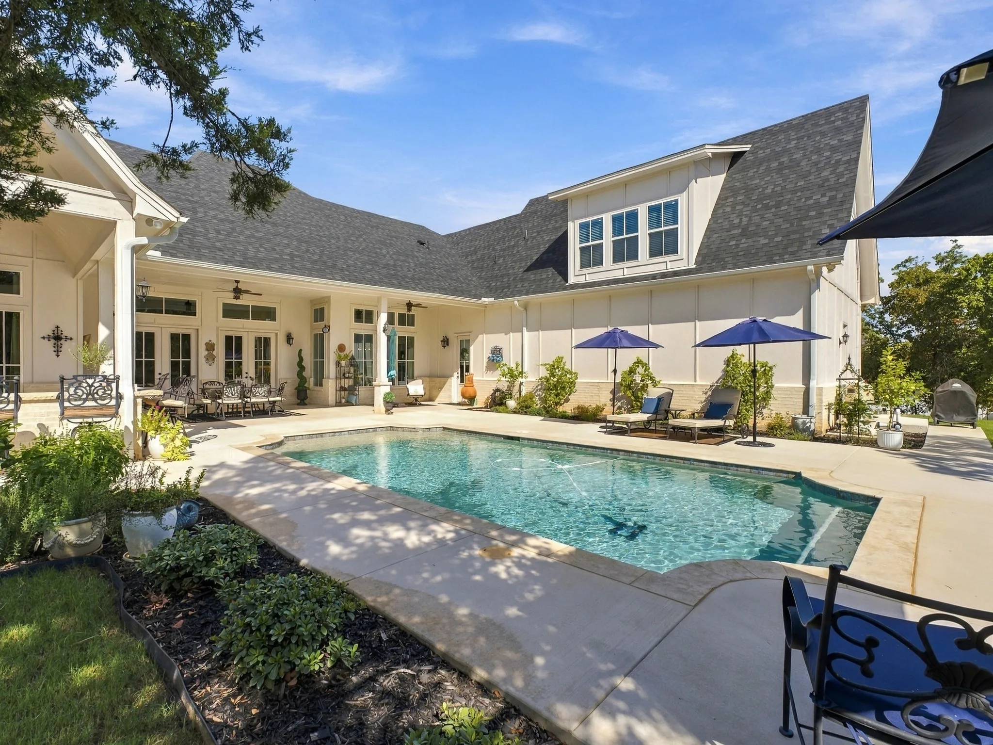 Expansive outdoor living area featuring a rectangular pool, concrete decking, and covered patio with multiple sets of French doors