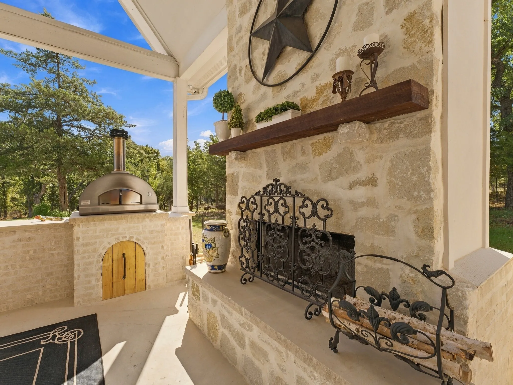 Covered patio featuring a stone fireplace, wood-fired oven, stone hearth, and a wood mantel