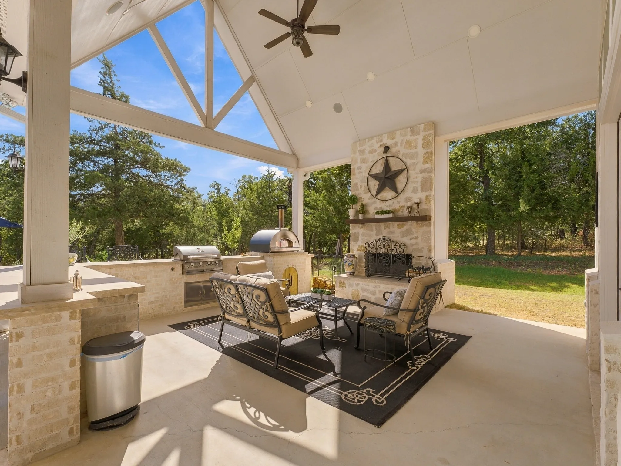 Expansive covered patio featuring a vaulted ceiling with exposed beams, stone fireplace, built-in outdoor kitchen, ceiling fan, and recessed lighting