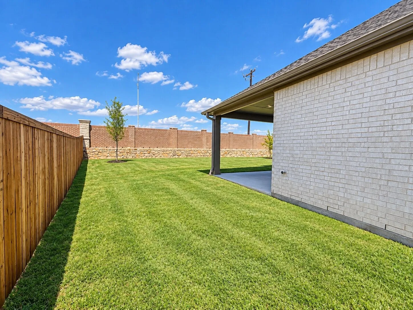 Expansive backyard with a manicured lawn, wood privacy fence, and a covered patio featuring a concrete surface