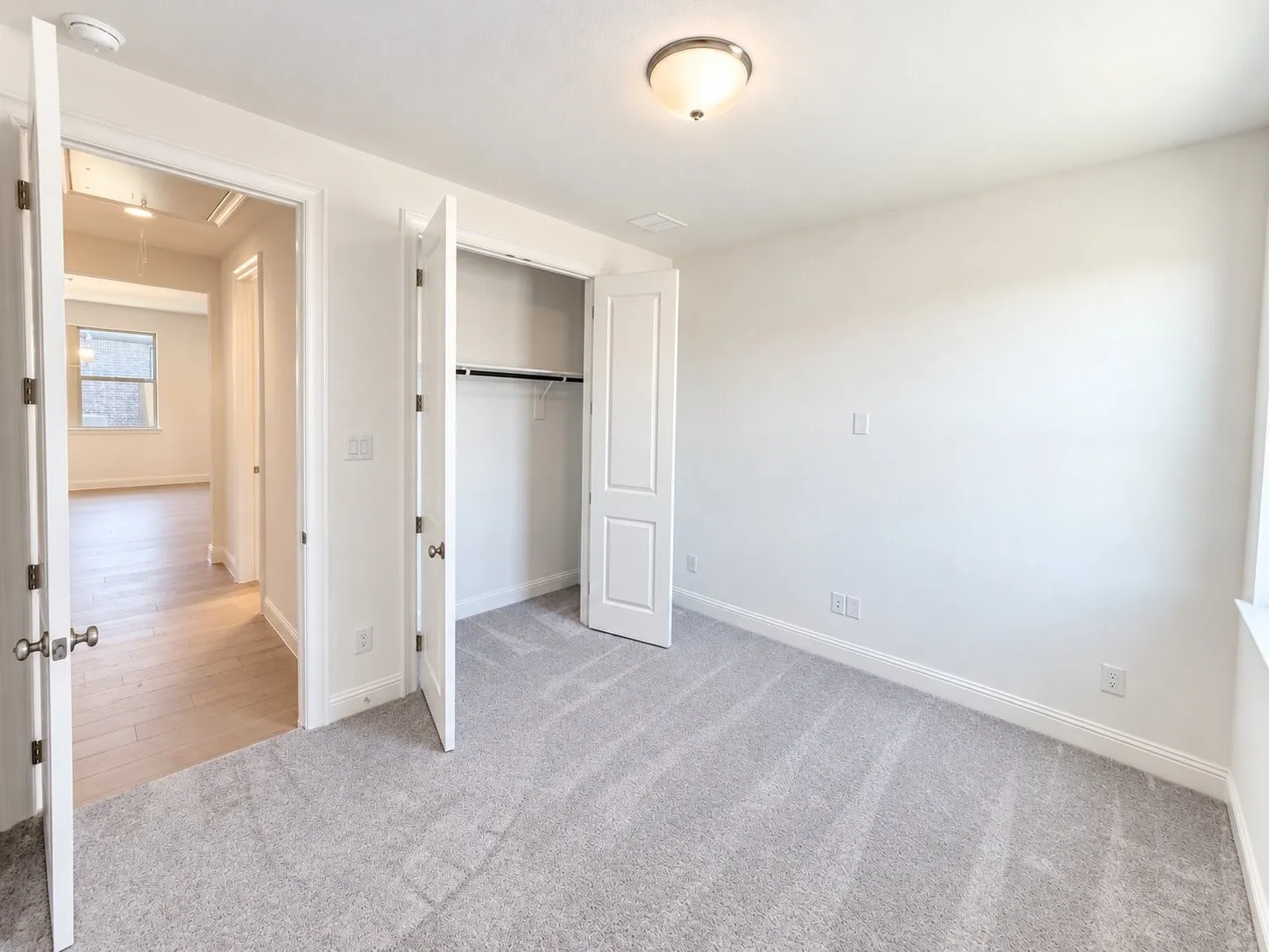 Neutral paint palette, flush mount ceiling light, light gray carpeting, bi-fold closet doors, and white trim