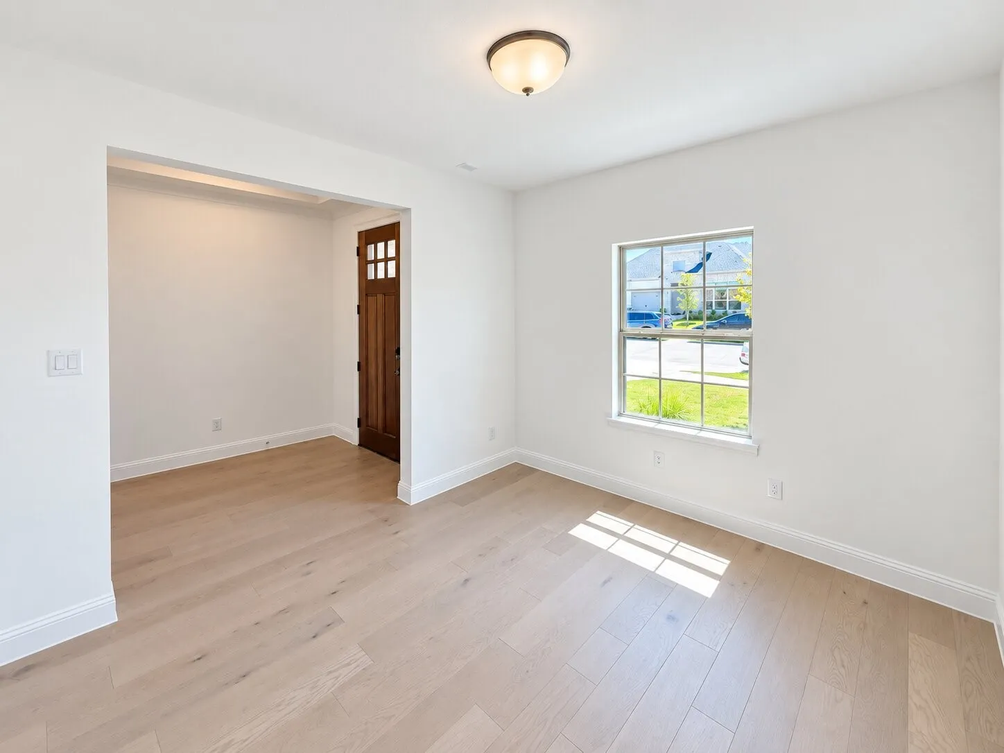Light wood-finish flooring, white painted walls, and a multi-pane window