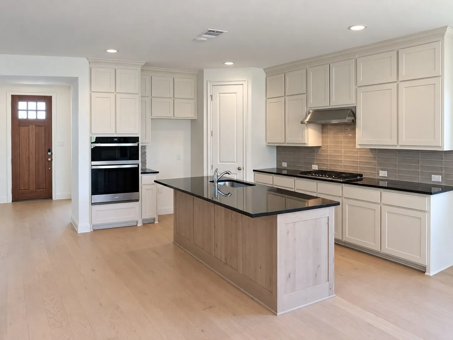 Modern kitchen with light wood-finish flooring, white cabinetry, dark countertops, a large center island, and a double wall oven