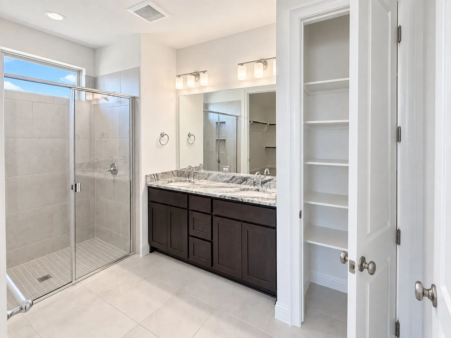 Glass-enclosed shower with tile surround, double vanity with stone countertop, dark wood-finish cabinetry, and built-in linen storage