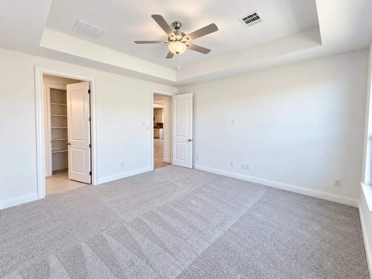 Spacious room featuring tray ceilings, neutral carpeting, and a ceiling fan with integrated lighting