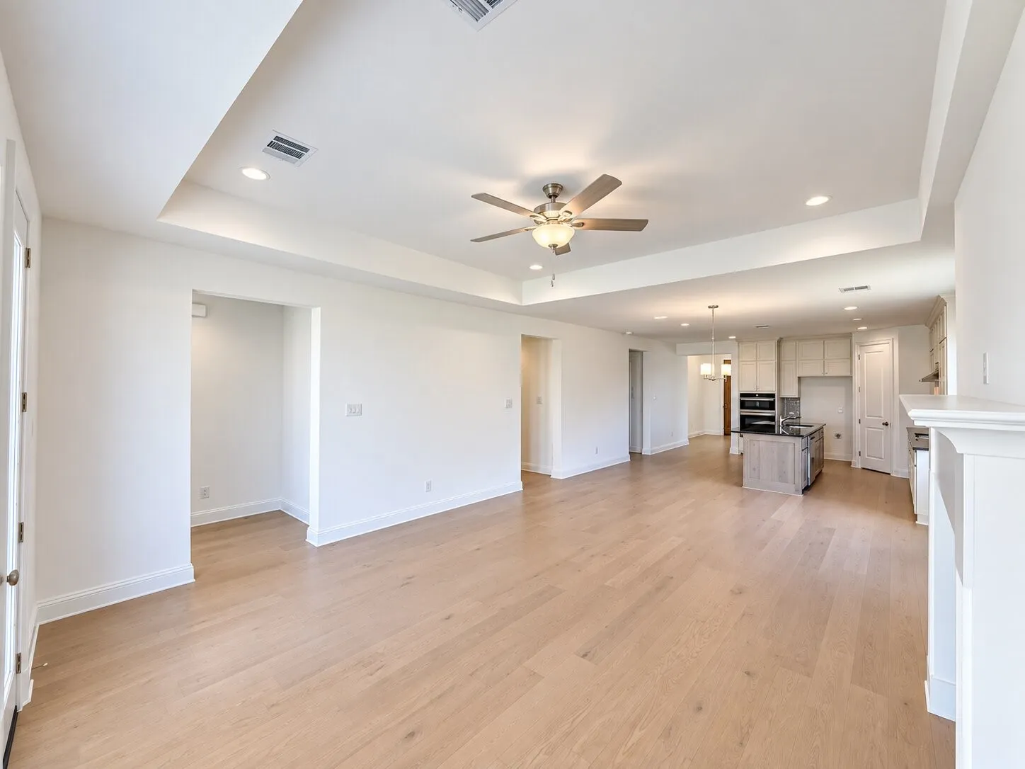 Expansive open-concept living area featuring wood-finish flooring, a tray ceiling with recessed lighting, and a ceiling fan