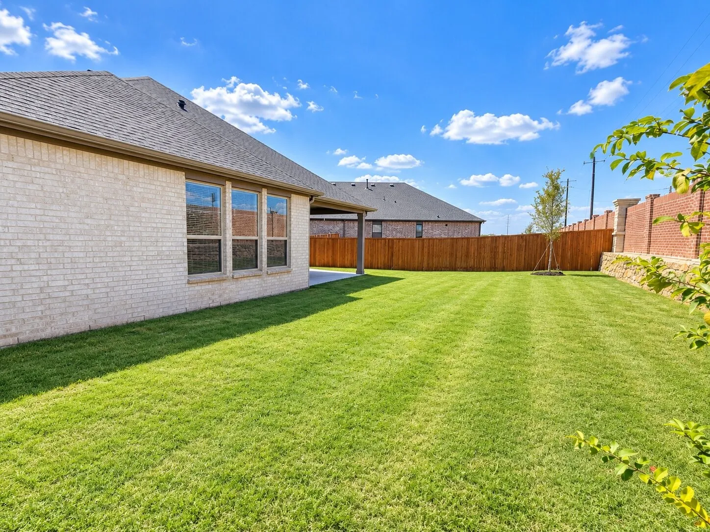Expansive backyard featuring a manicured lawn, full privacy fence, and brick retaining wall