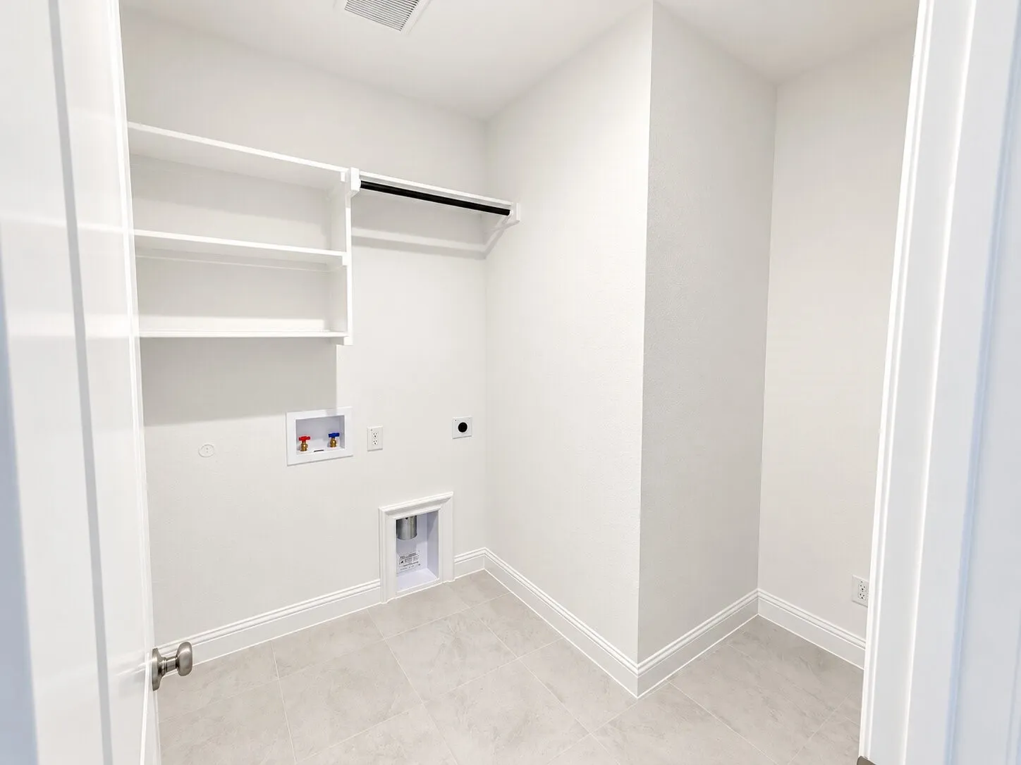 Laundry area featuring built-in shelving, a clothes hanging rod, and light-toned tile flooring