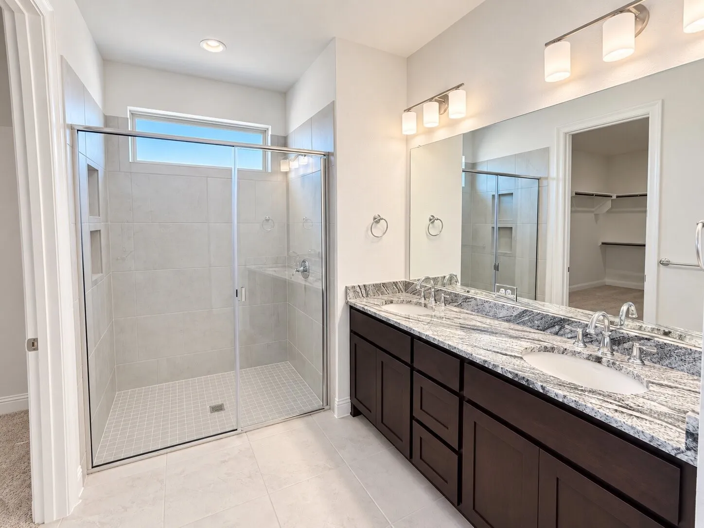 Walk-in shower with clear glass enclosure, dual vanity with undermount sinks, stone countertops, and dark wood cabinetry