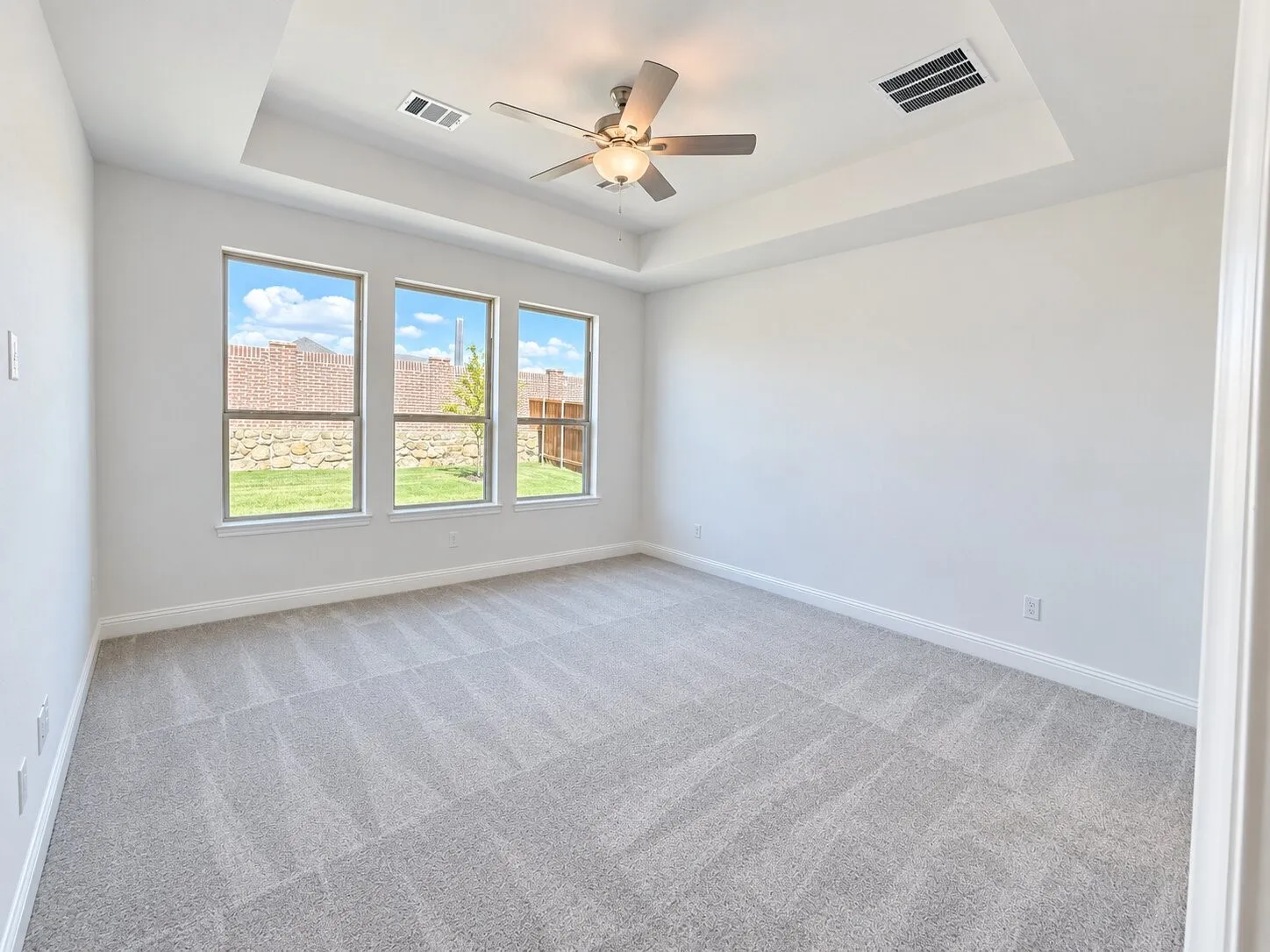 Recessed ceiling with a central fan, light gray carpeting, triple windows, and neutral wall tones