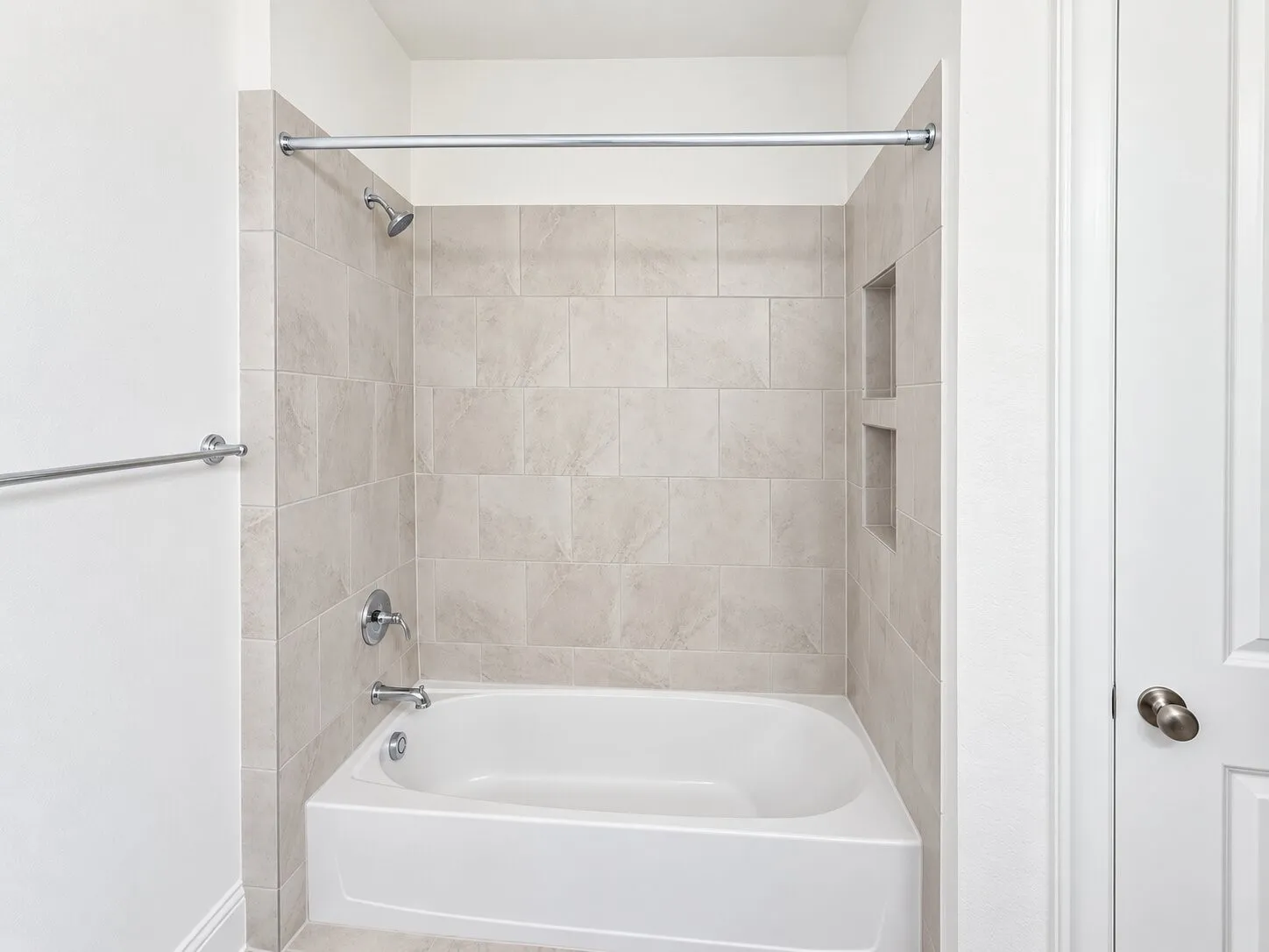 Bathtub with tiled surround, chrome fixtures, and integrated storage niches