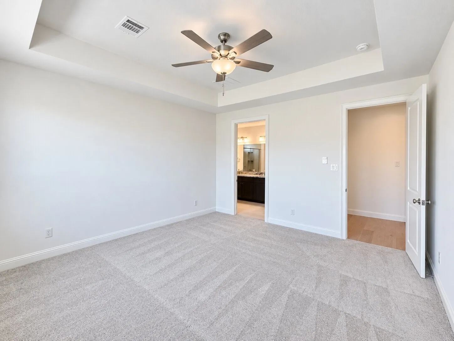 Tray ceiling with a ceiling fan, light gray carpet, and two doorways