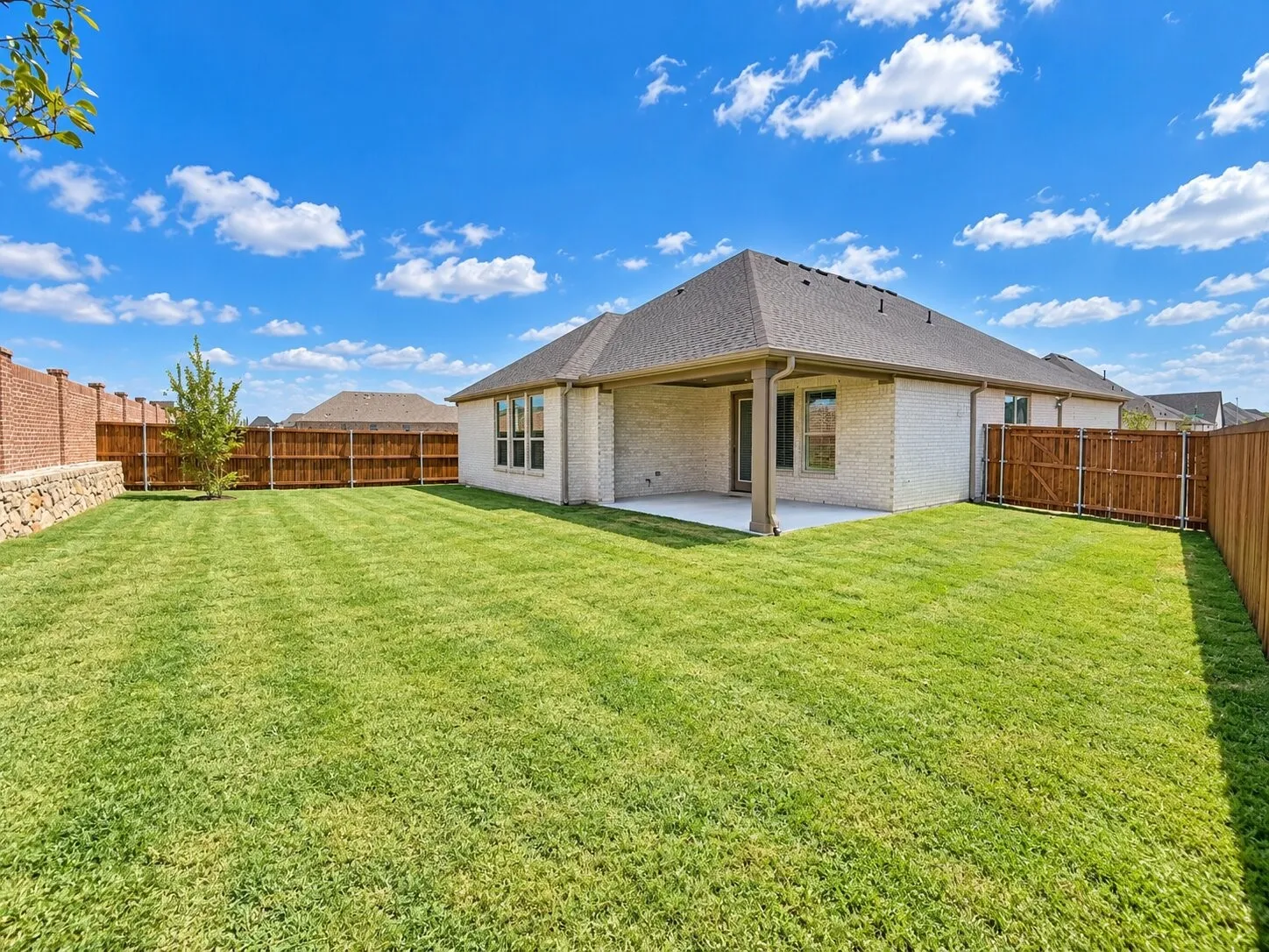 Expansive backyard featuring a manicured lawn, full wood fencing, and a covered patio area