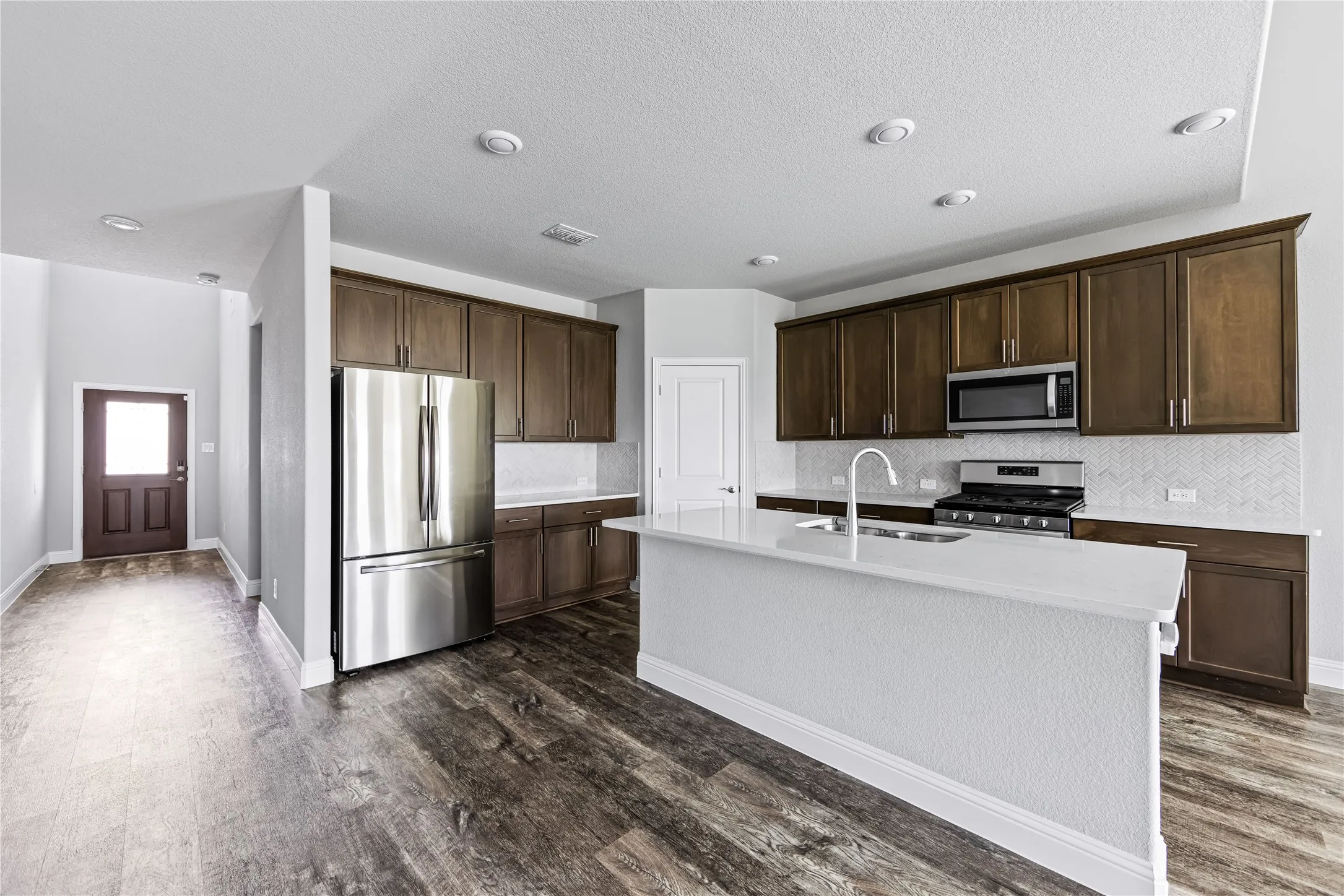 Kitchen featuring dark wood-finish cabinetry, stainless steel appliances, a white herringbone tile backsplash, and a central island with a white countertop
