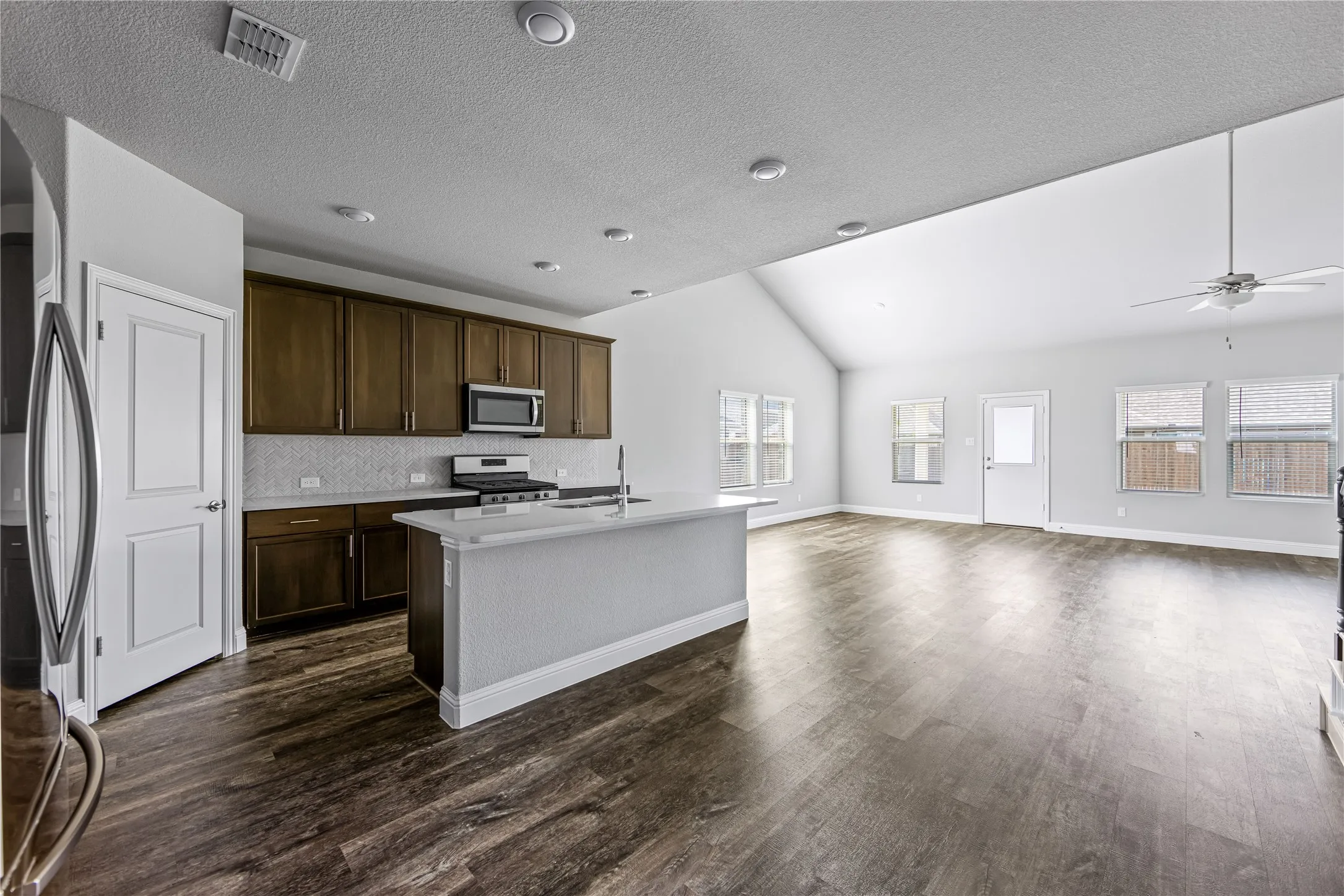 Vaulted ceiling, recessed lighting, wood-finish flooring, white kitchen island with undermount sink, and dark wood cabinetry with stainless steel appliances