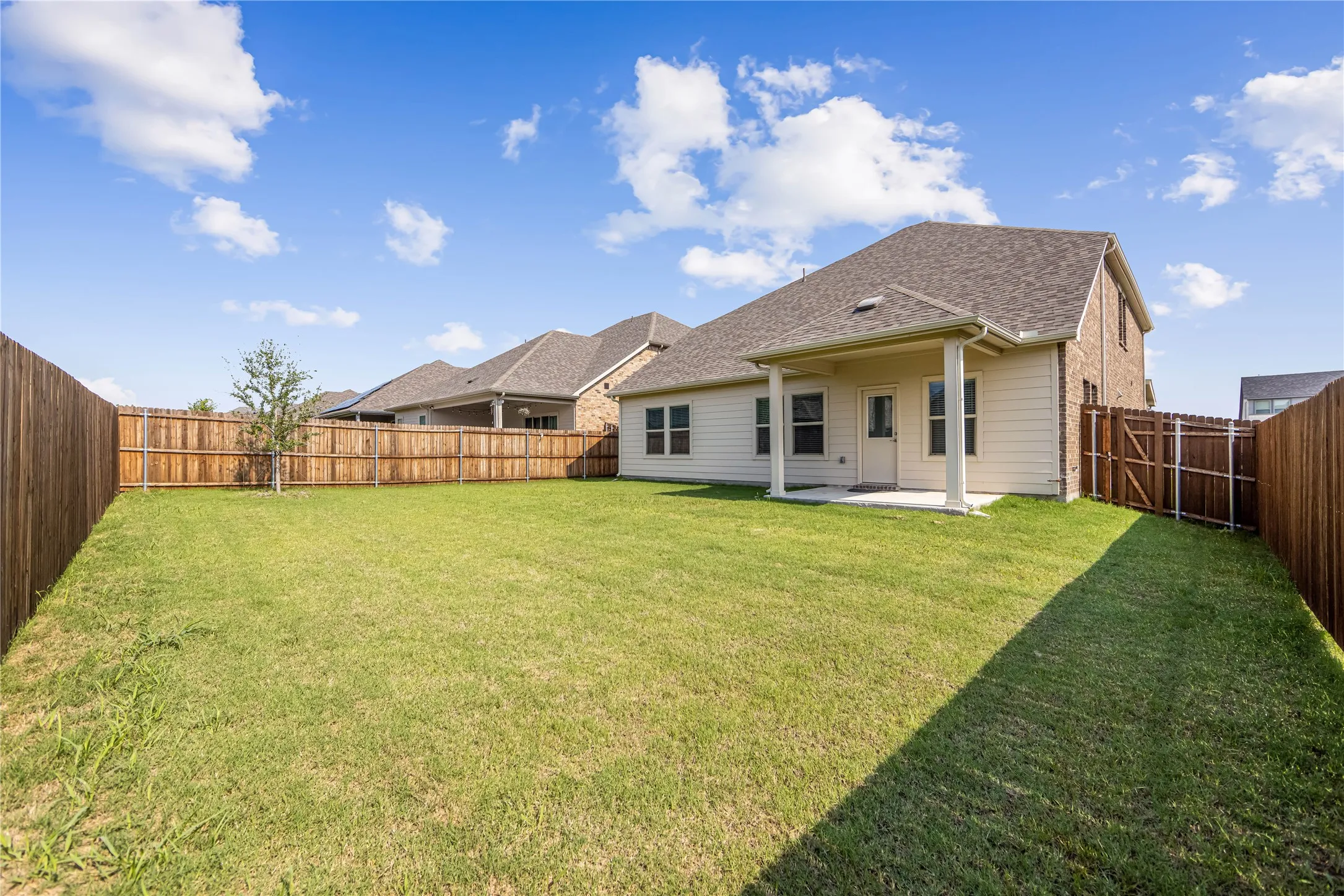 Expansive backyard with a covered patio, wood fencing, and a mature tree