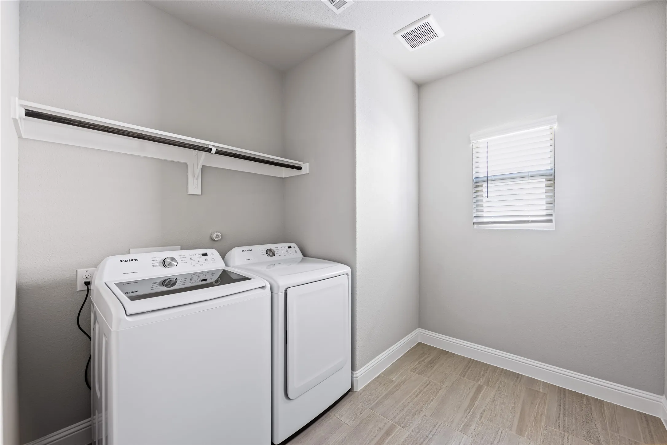 Dedicated utility space featuring a built-in shelf with hanging rod, a window with horizontal blinds, and wood-finish tile flooring