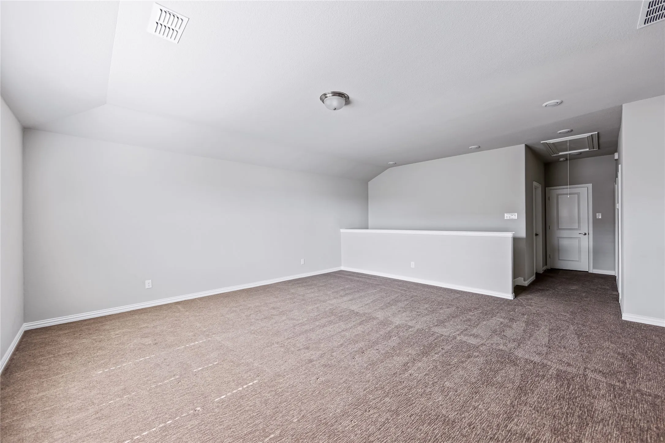 Spacious loft area featuring neutral-toned carpeting and walls, a partial wall partition, and a flush mount ceiling light