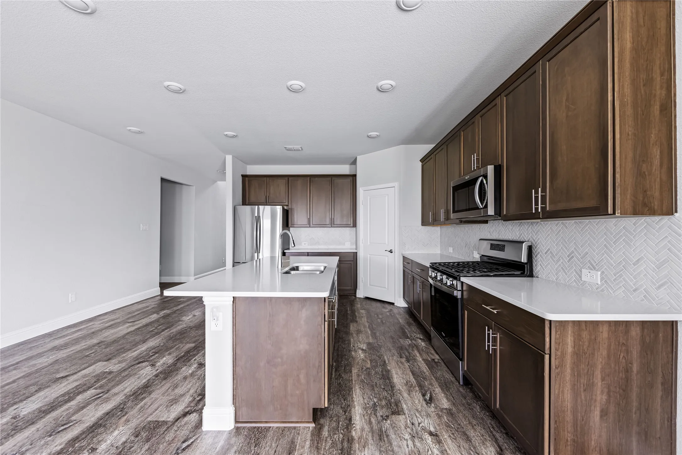 Spacious kitchen featuring wood-finish cabinetry, white countertops, stainless steel appliances, and a herringbone tile backsplash