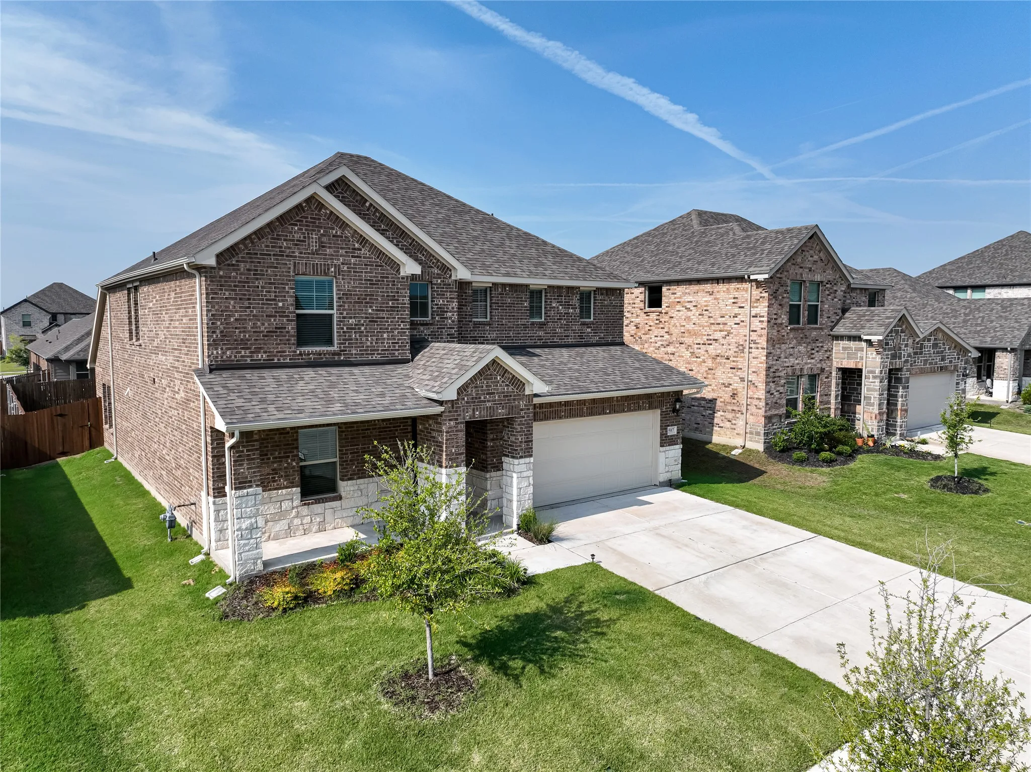 Two-story brick exterior with stone accents, covered entry, attached garage, and concrete driveway